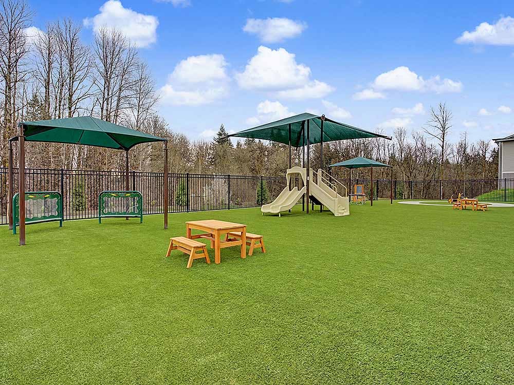 Playground with green turf, slides, shaded areas, and picnic tables