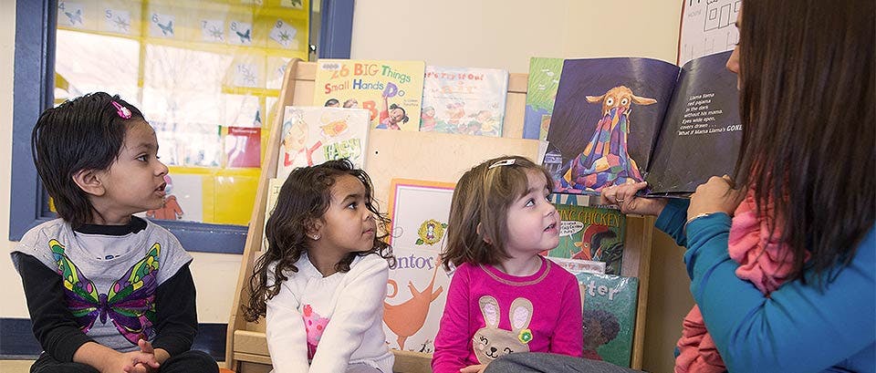 Adult reading a book to three children in a classroom