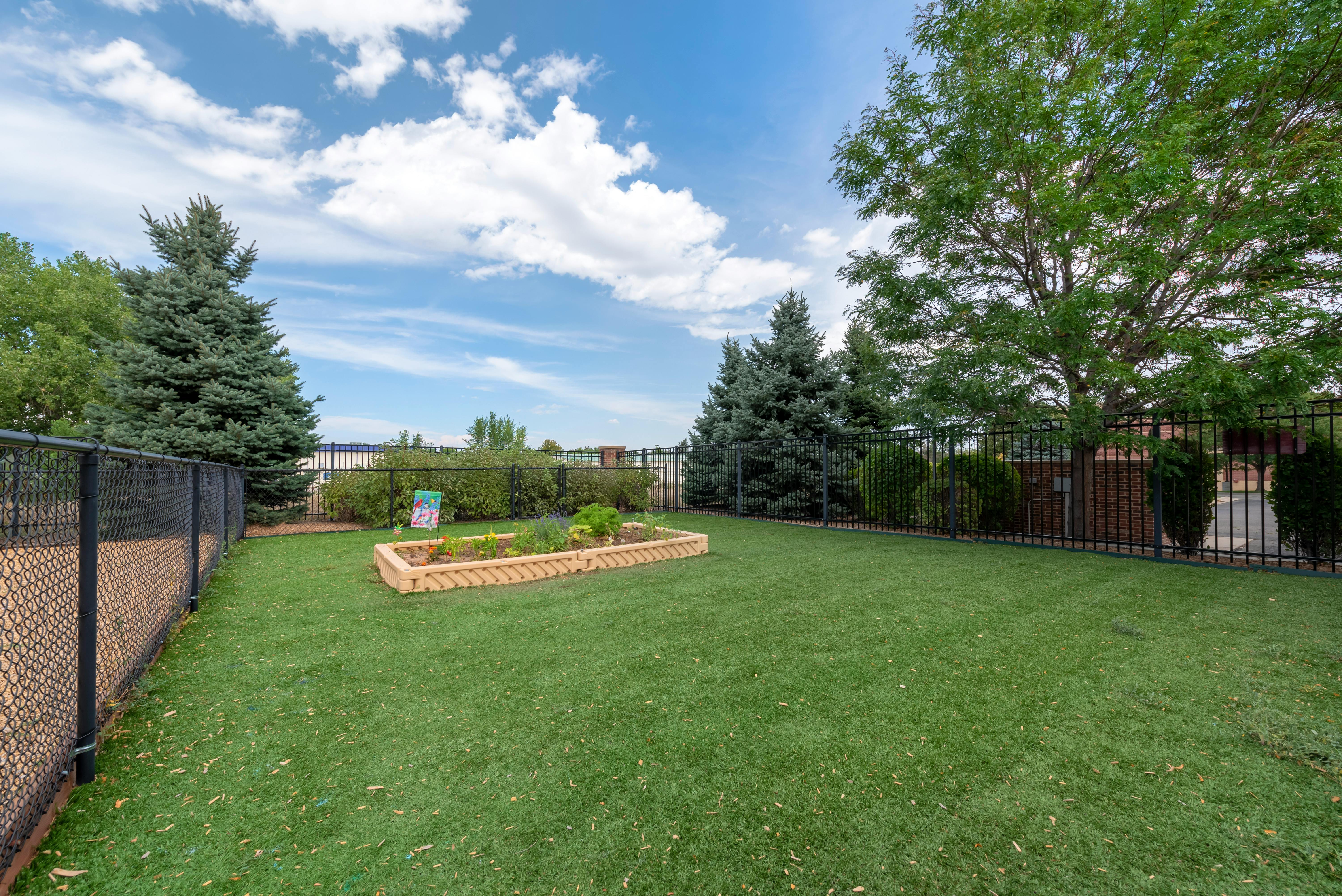 An outdoor play area with artificial turf, surrounded by fences and trees