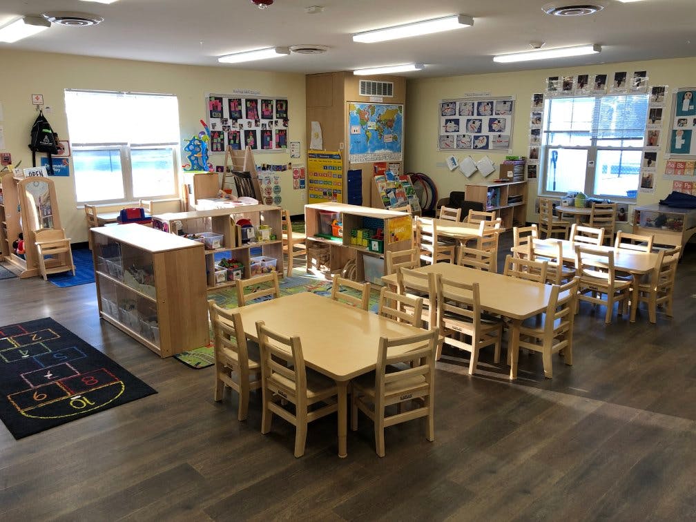 An empty classroom with small tables, chairs, and learning materials