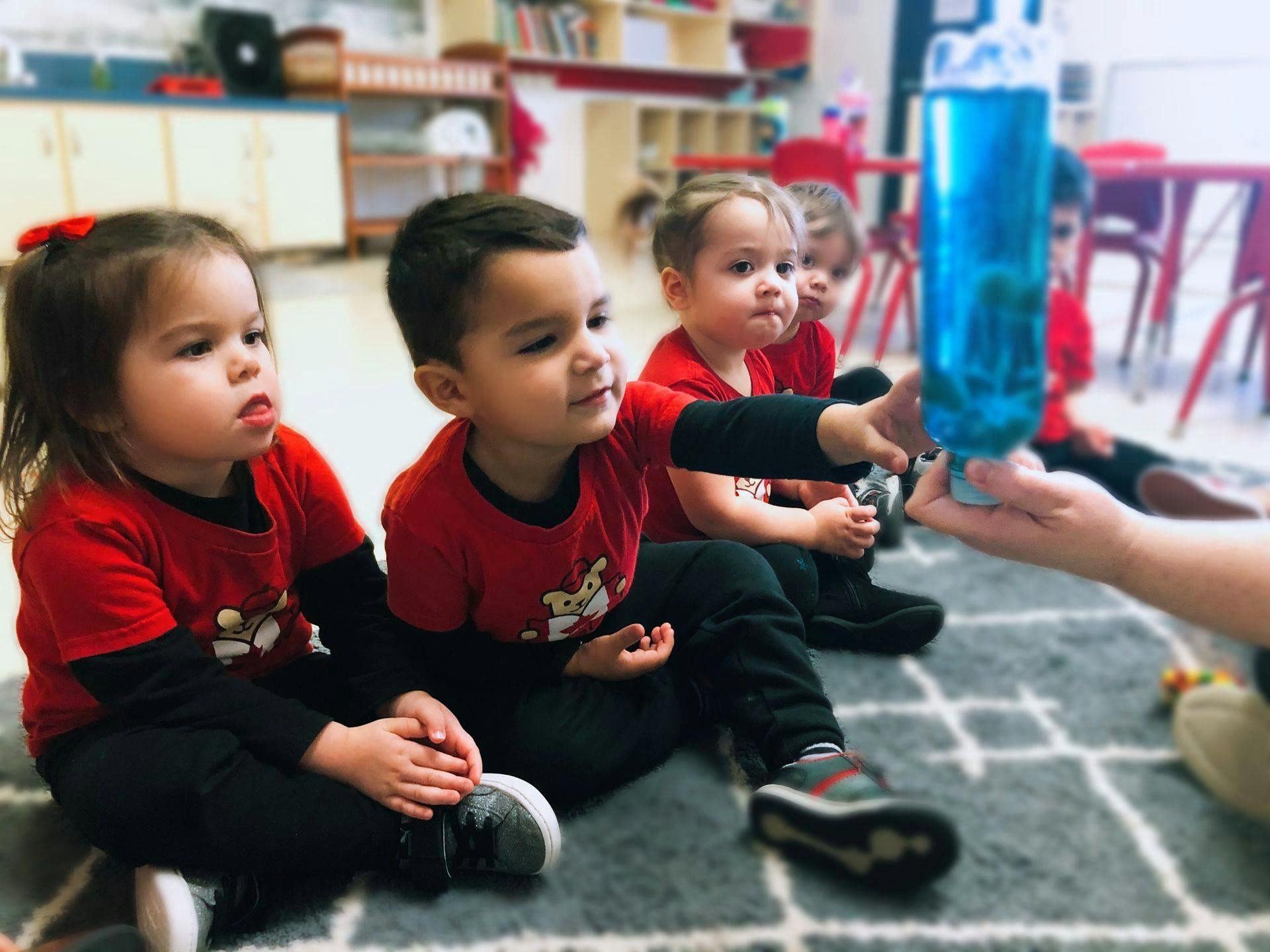 Children sitting on floor looking at a blue bottle