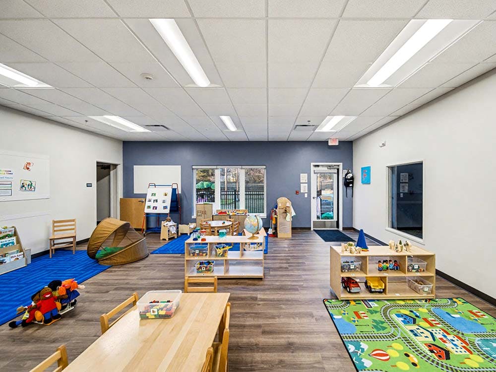 Classroom with small tables, chairs, colorful rugs, and toys