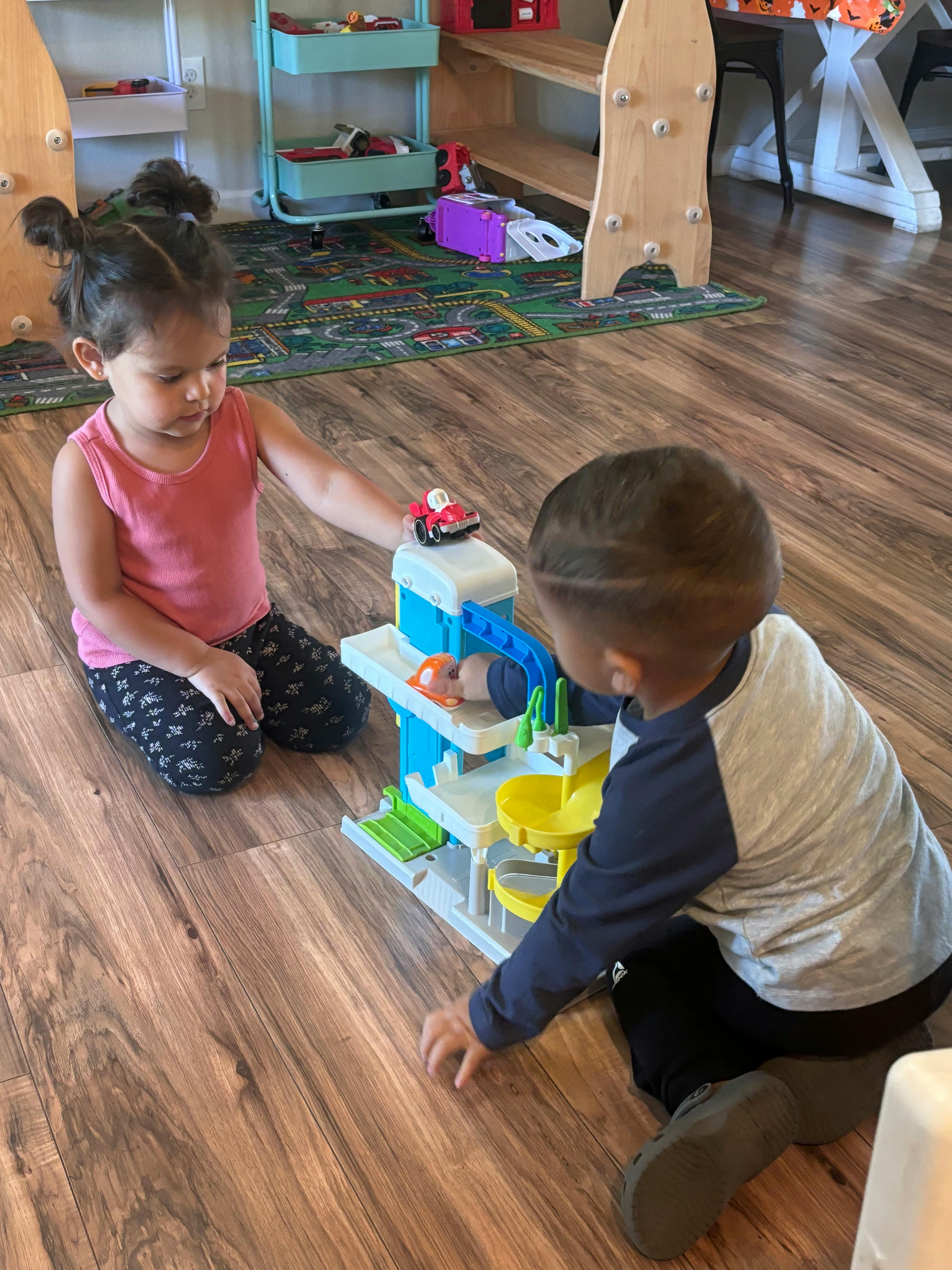 Two children playing with a toy car garage on a wooden floor