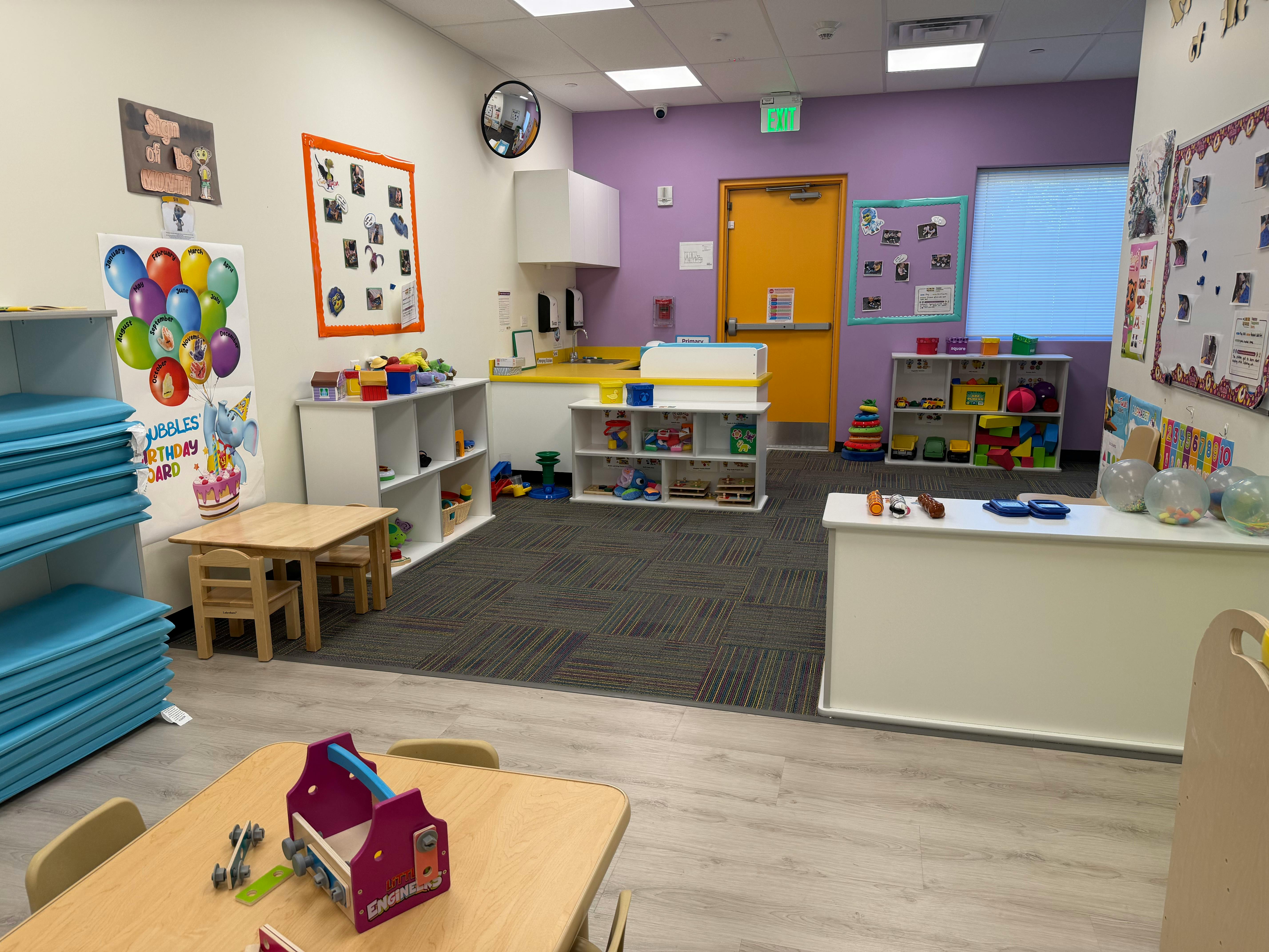 Classroom with child-sized tables and chairs, cubbies, play area, and a sink
