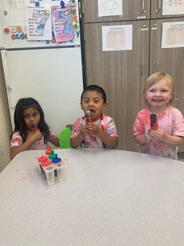 Three children eating popsicles at a table