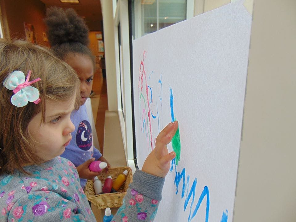 Child painting on a large white paper with another child watching