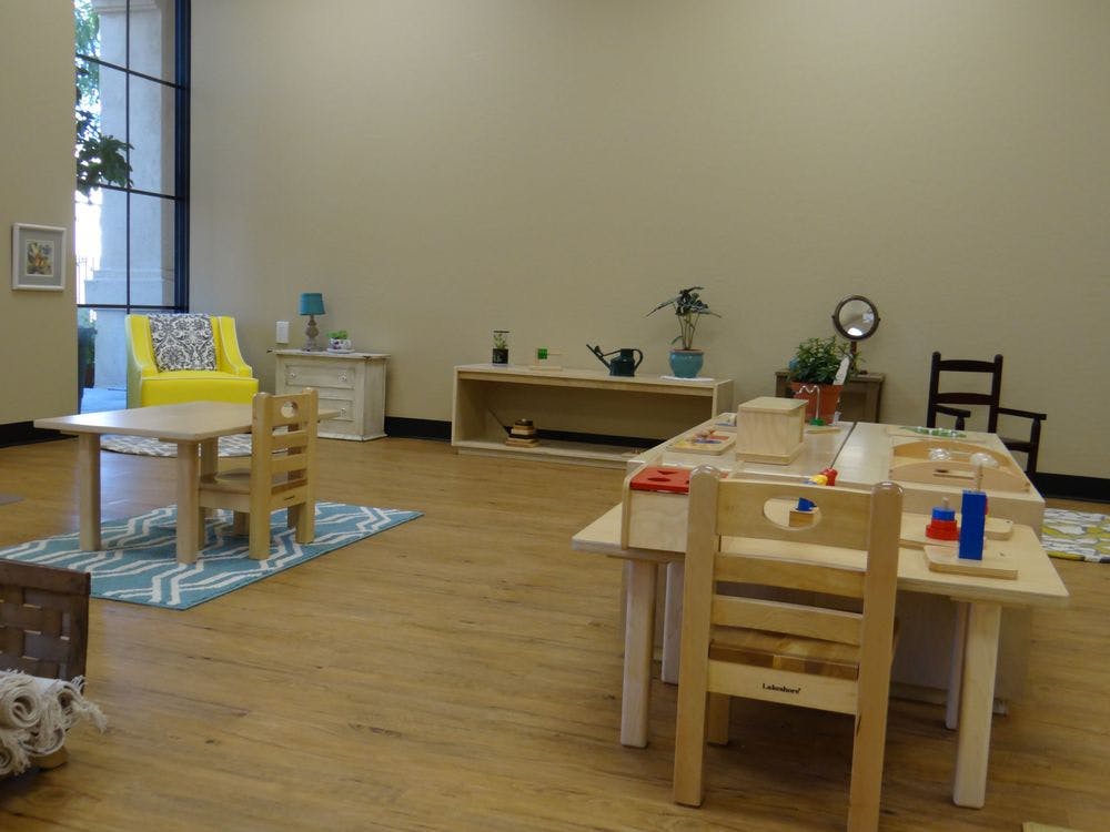Classroom with small tables and chairs, a yellow armchair, and shelves