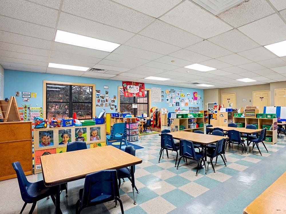 Empty classroom with tables and chairs, artwork on walls, and toys on shelves