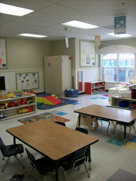 Classroom with child-sized tables and chairs, shelves of toys, and colorful rugs