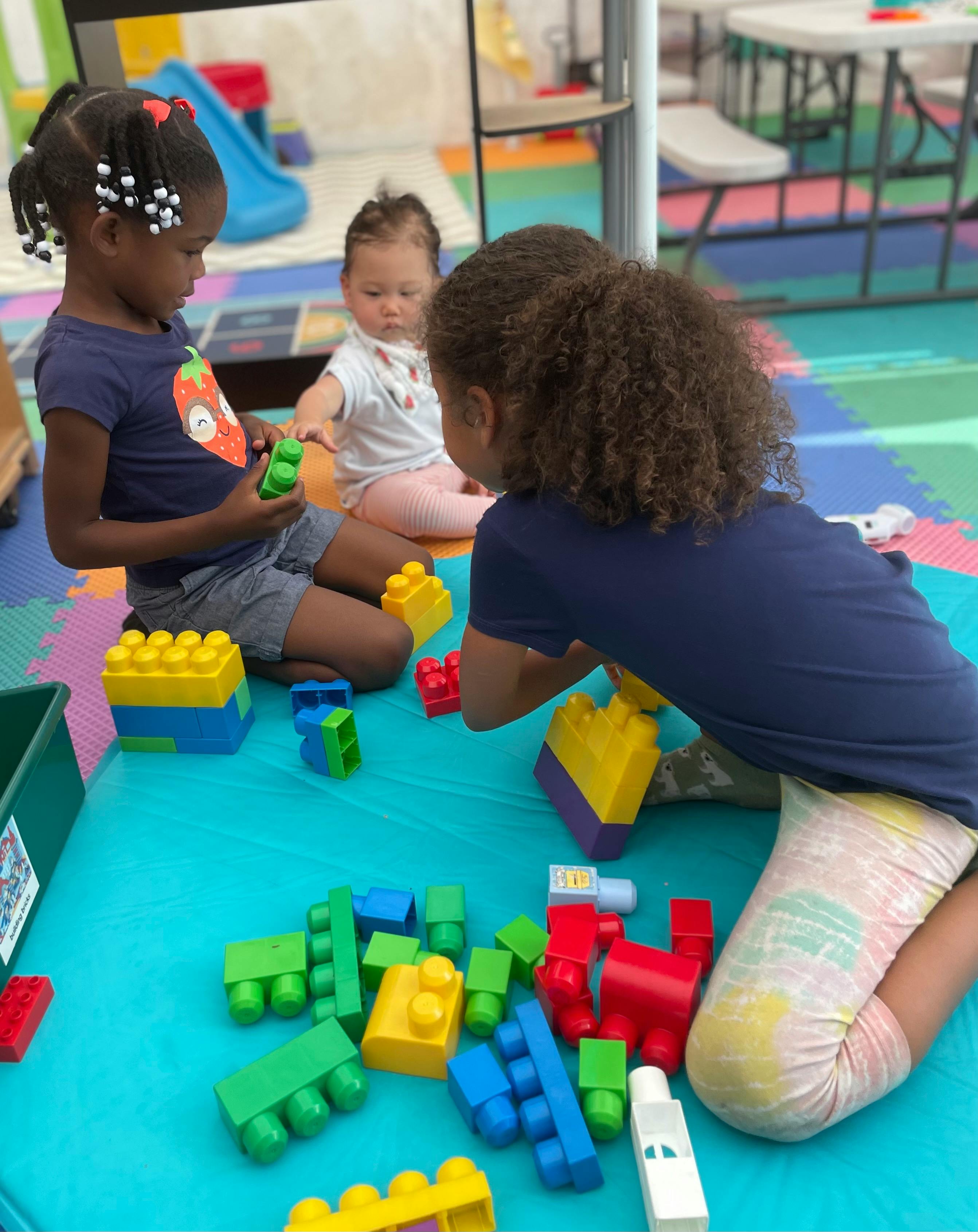 Three children playing with colorful building blocks on a mat