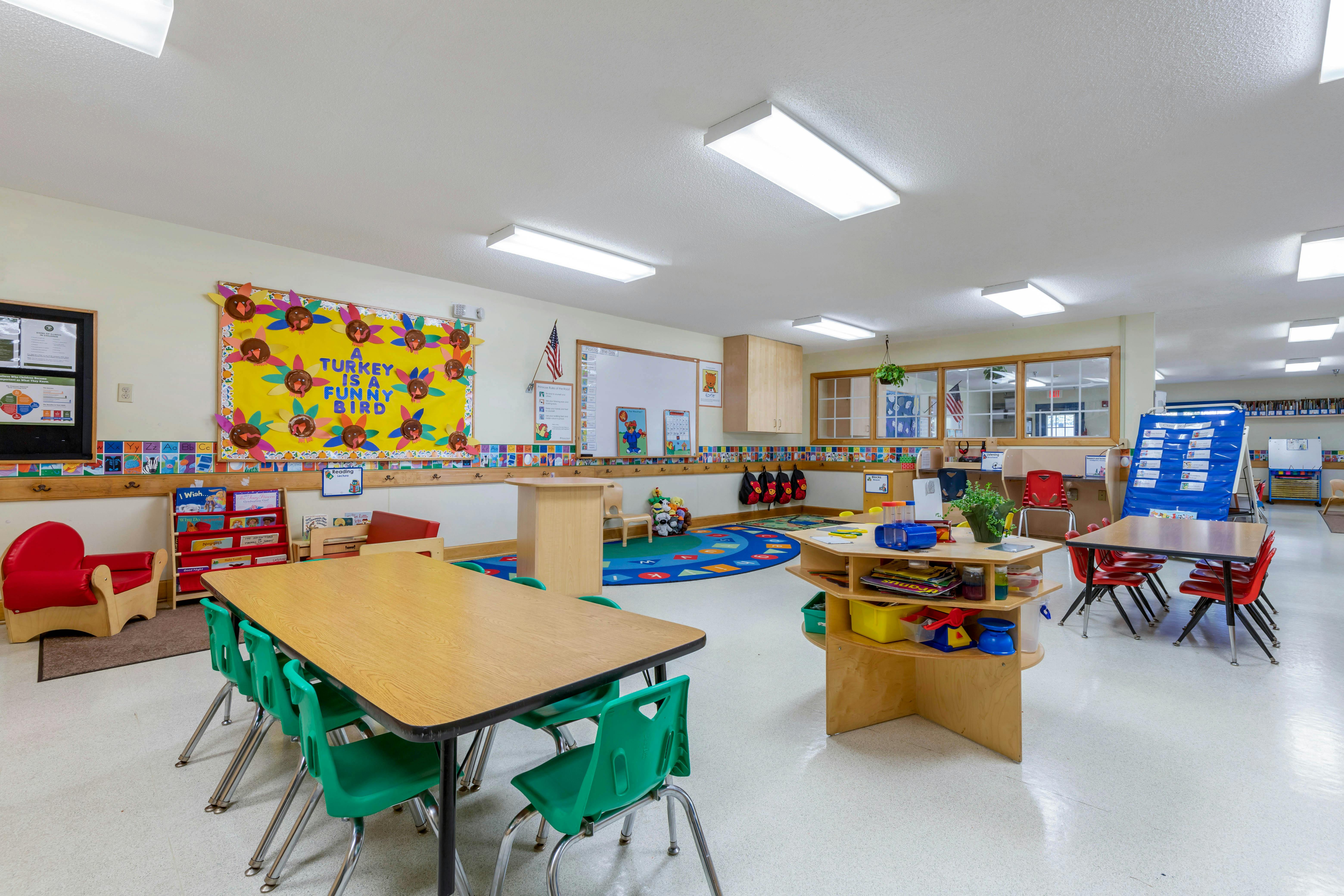 A classroom with tables, chairs, a reading corner, and a bulletin board that says "A Turkey Is A Funny Bird"