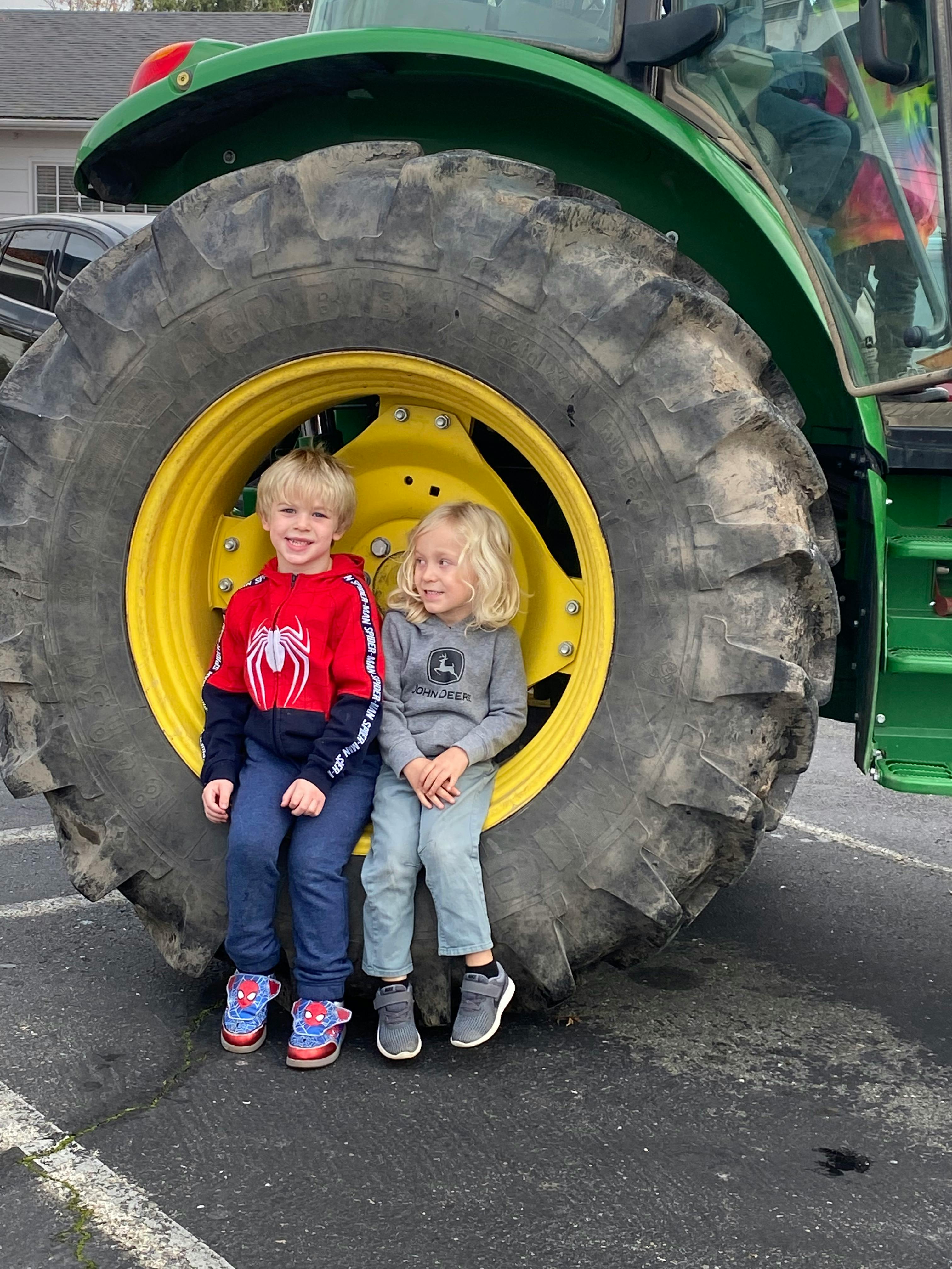 Two children sitting in front of a large tractor tire