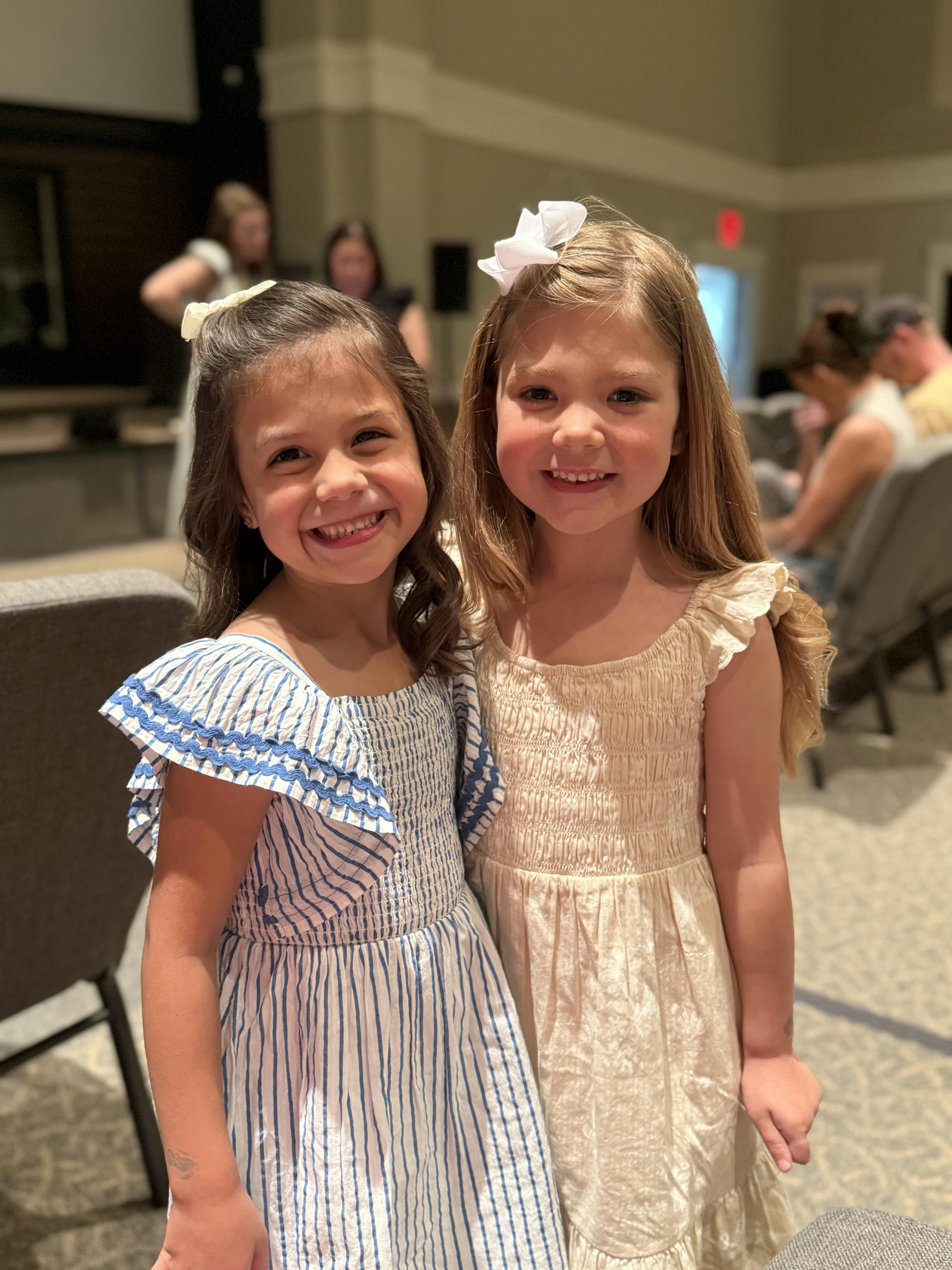 Two children wearing dresses smiling in an indoor setting