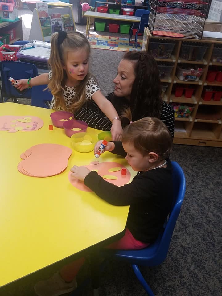 Adult and two children doing crafts at a table in a classroom