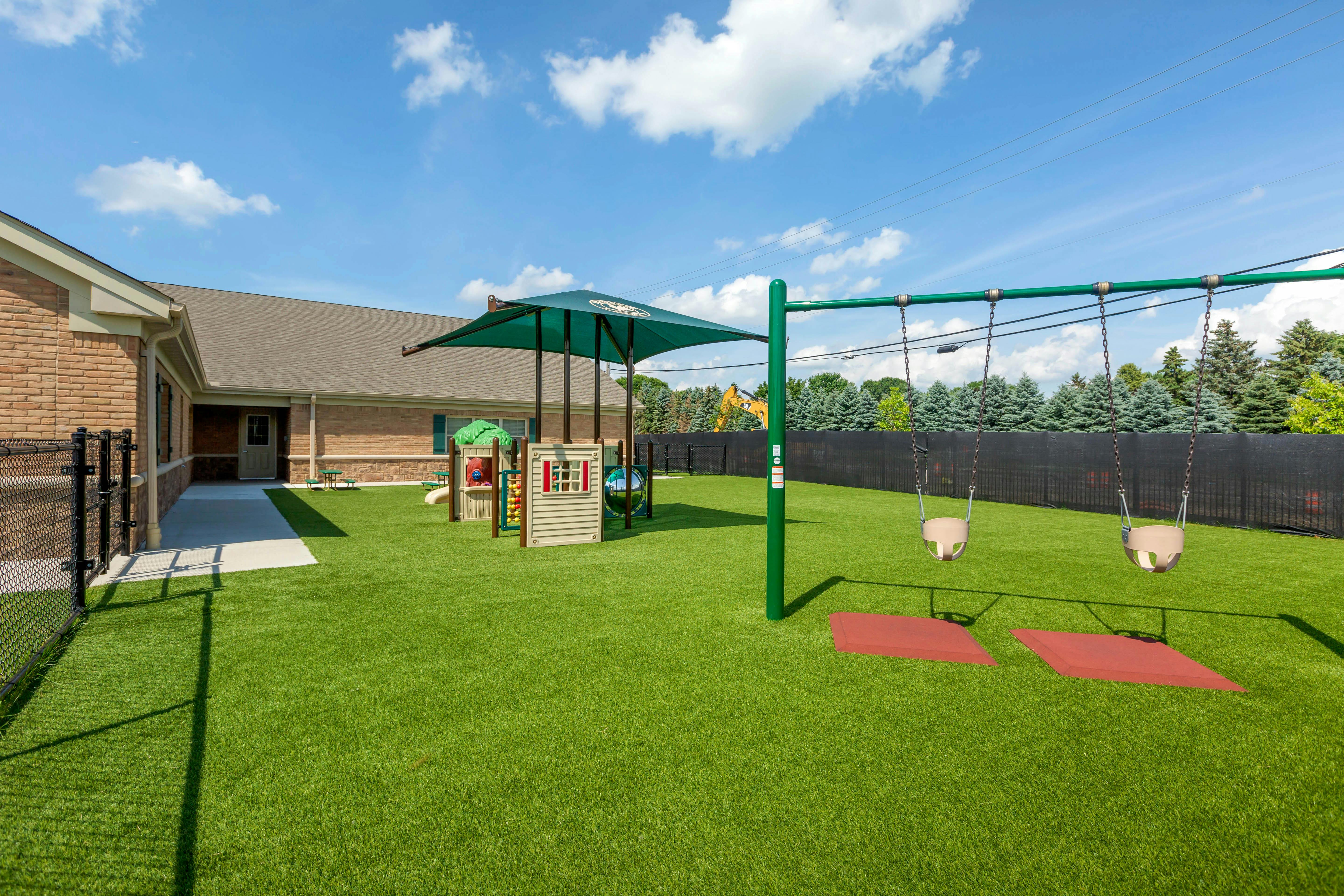 Outdoor playground with artificial turf, swing set, and play structure under a shade