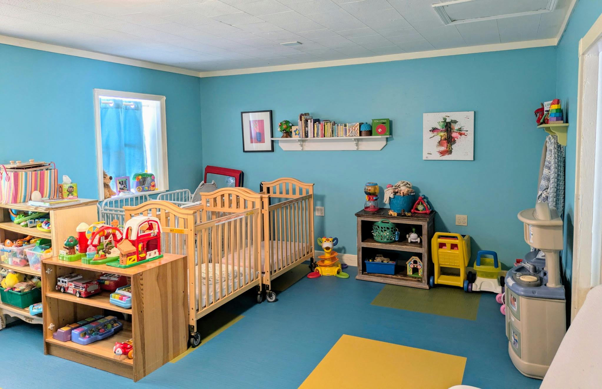 Bright child care room with wooden cribs, shelving units, and assorted toys