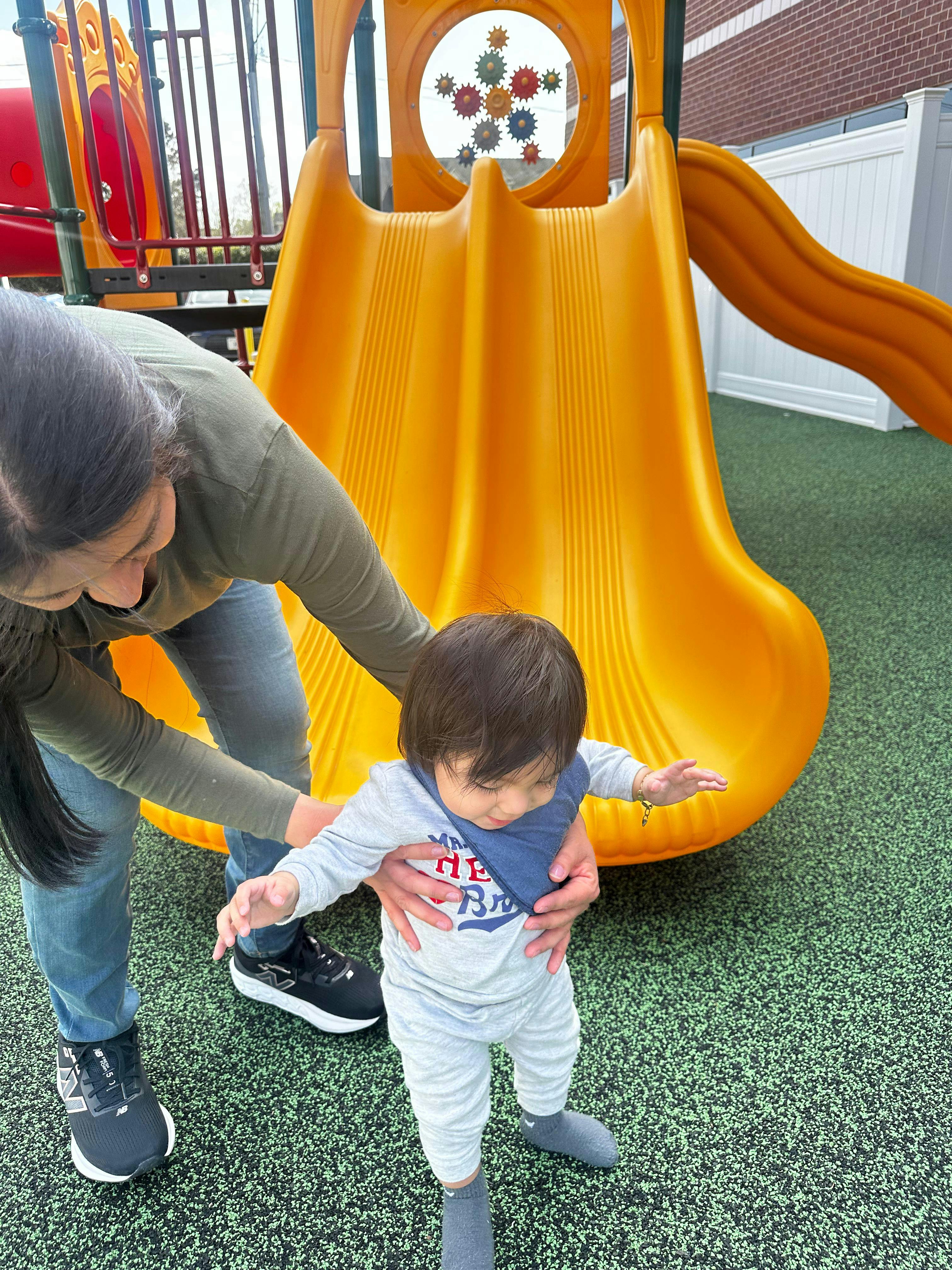 Person supporting a toddler on a playground