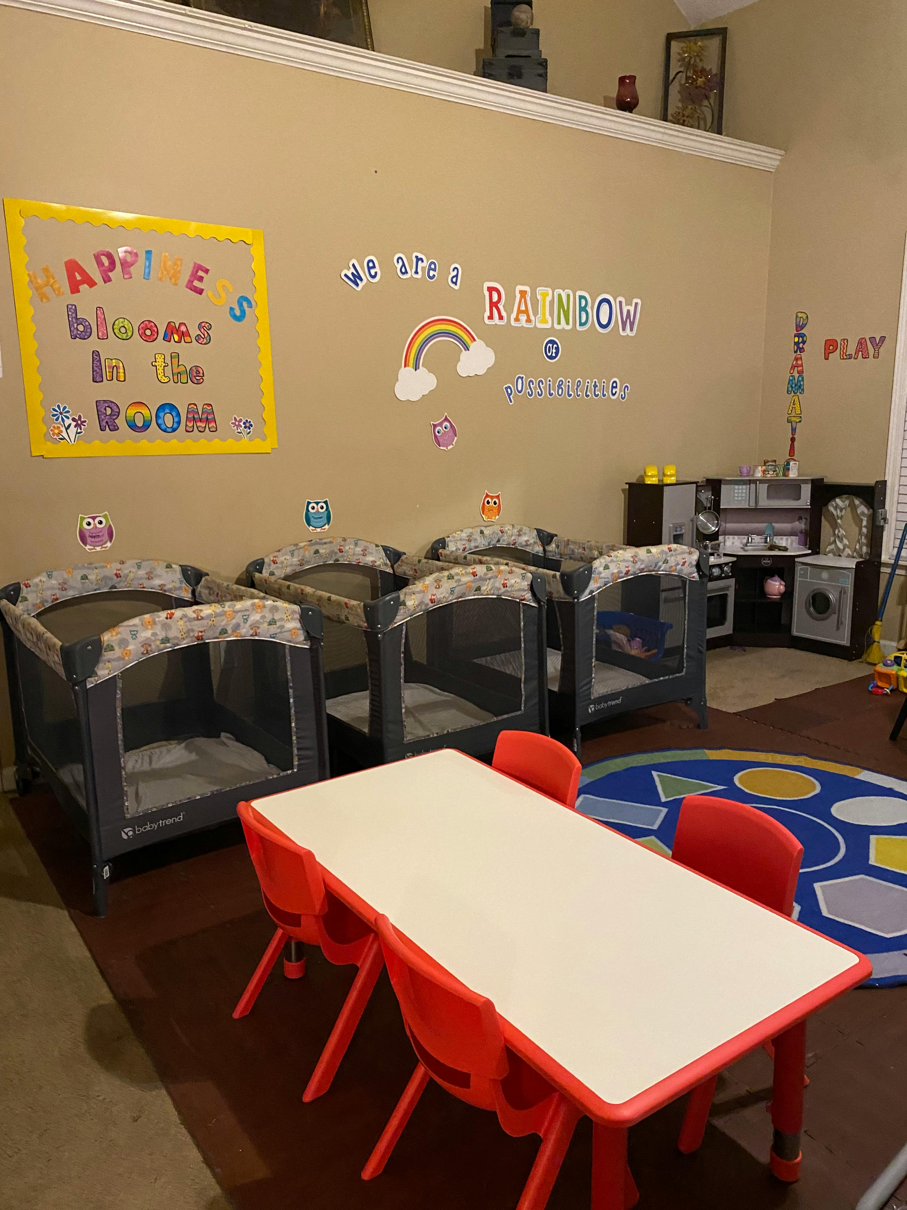 Daycare room with multiple cribs, a child-sized table and chairs, and wall decorations