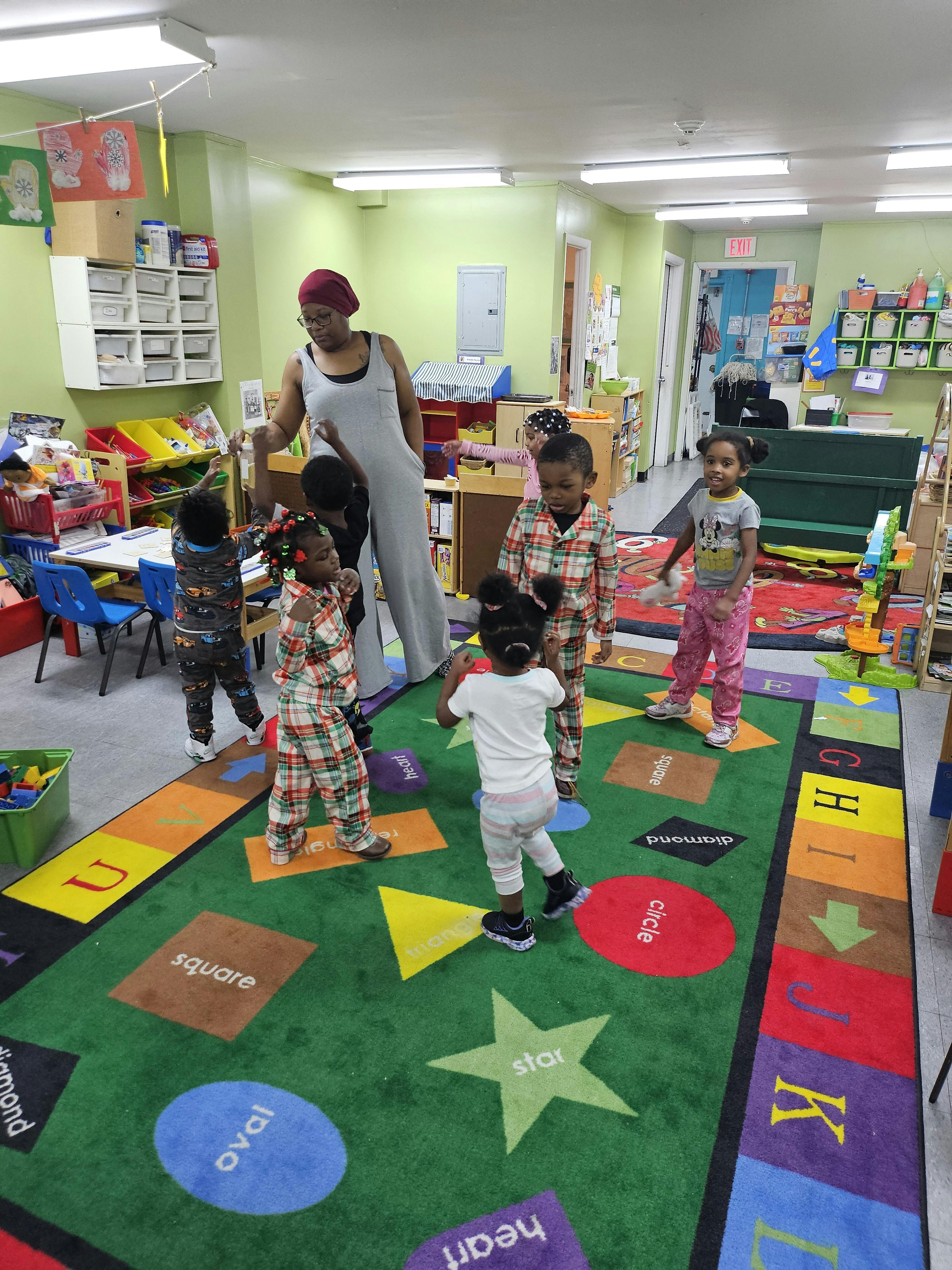 Adult and children standing on a colorful rug with shapes and letters in a classroom
