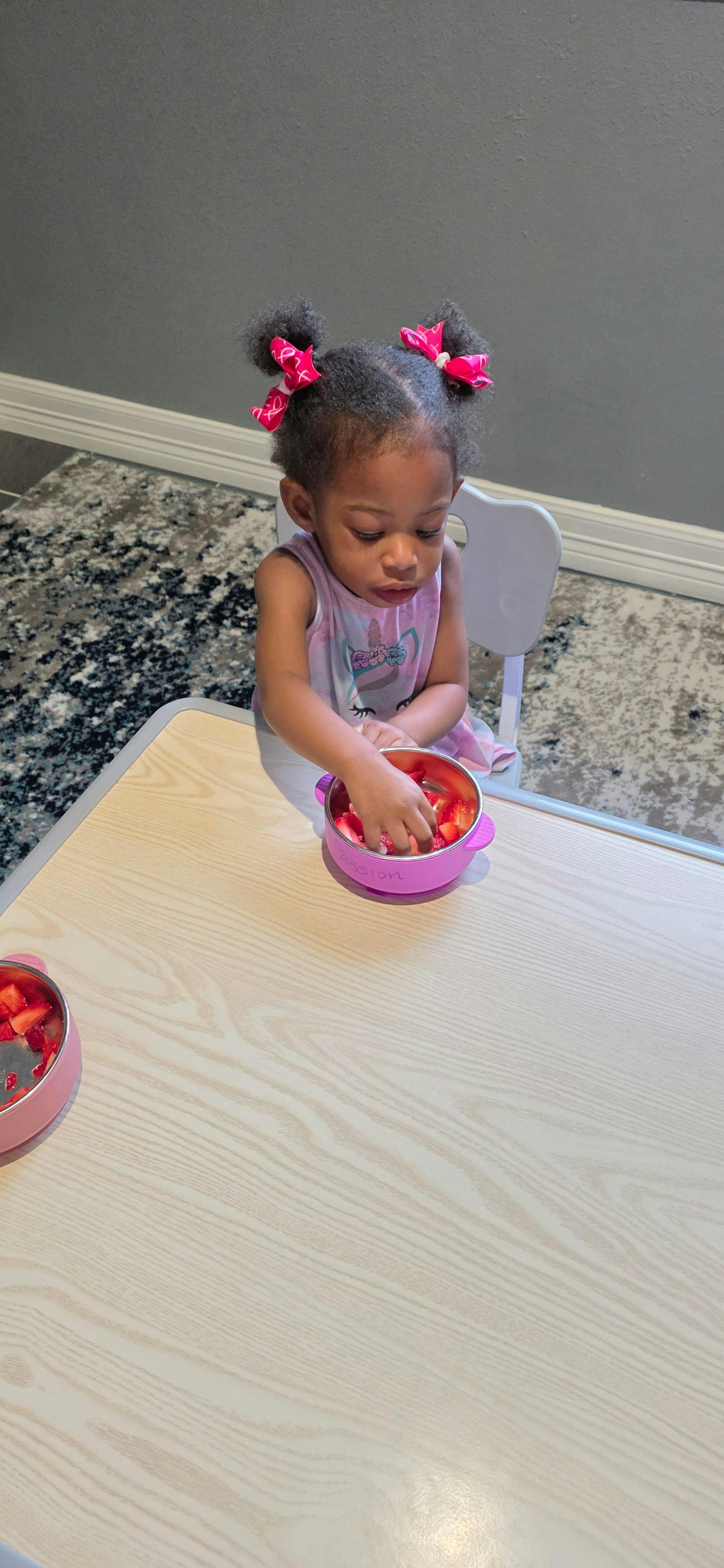 child reaching into a bowl of cut strawberries on a table