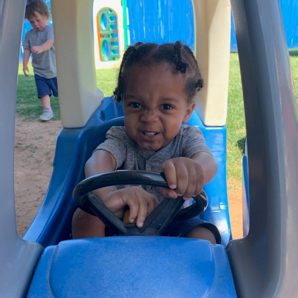 Child in a toy car holding the steering wheel