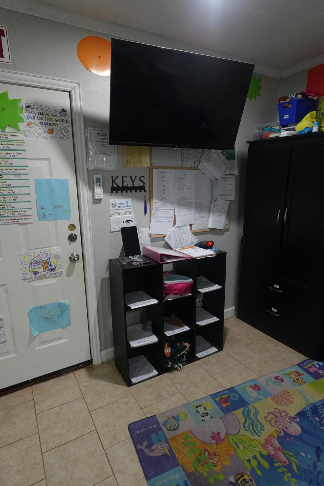 Wall-mounted television above a storage unit with a door and rug
