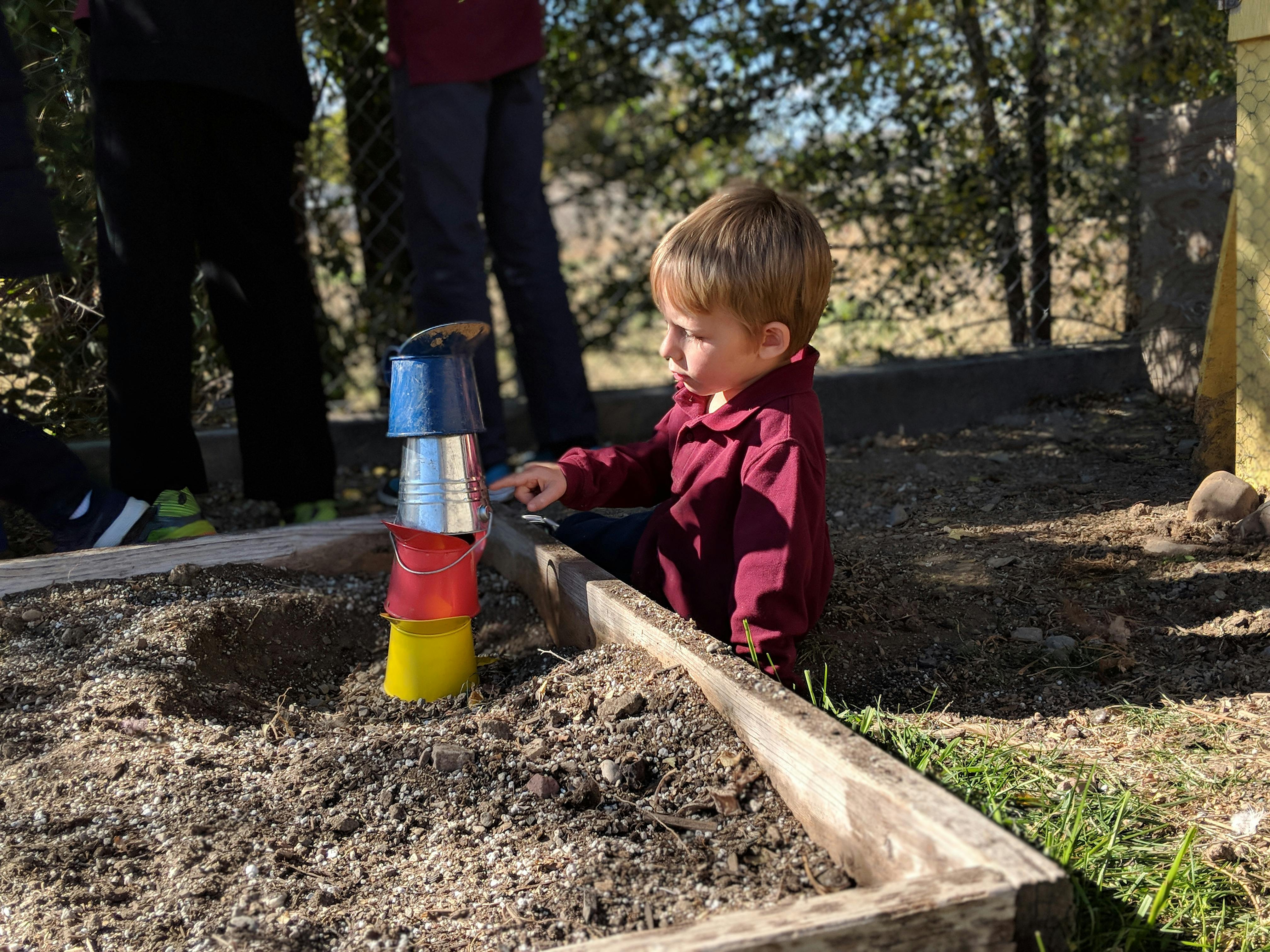 Child playing with stacking cups in a garden bed