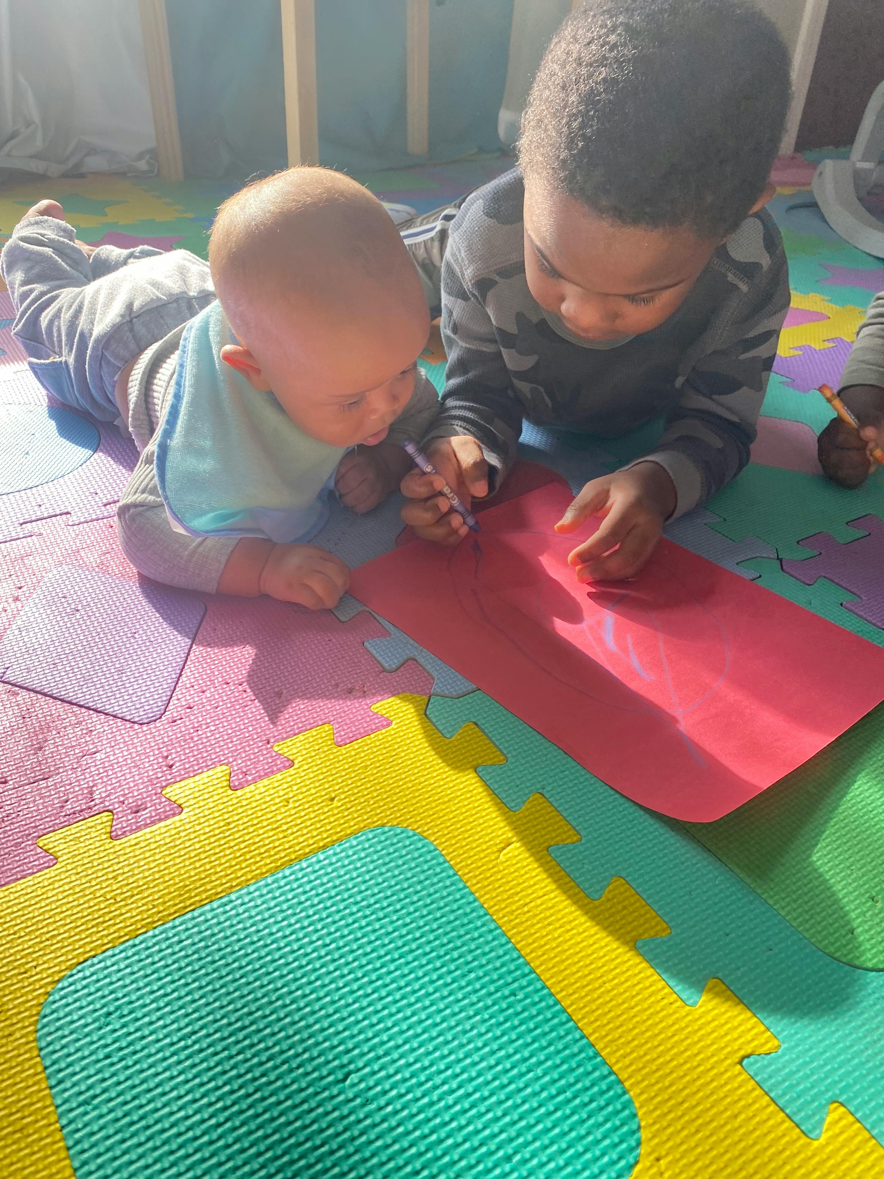 Two children drawing on a red paper on a colorful mat