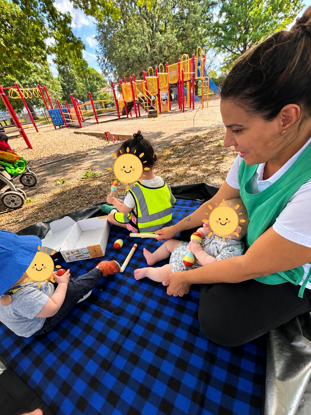 Adult and children playing with wooden toys on a blanket at a playground