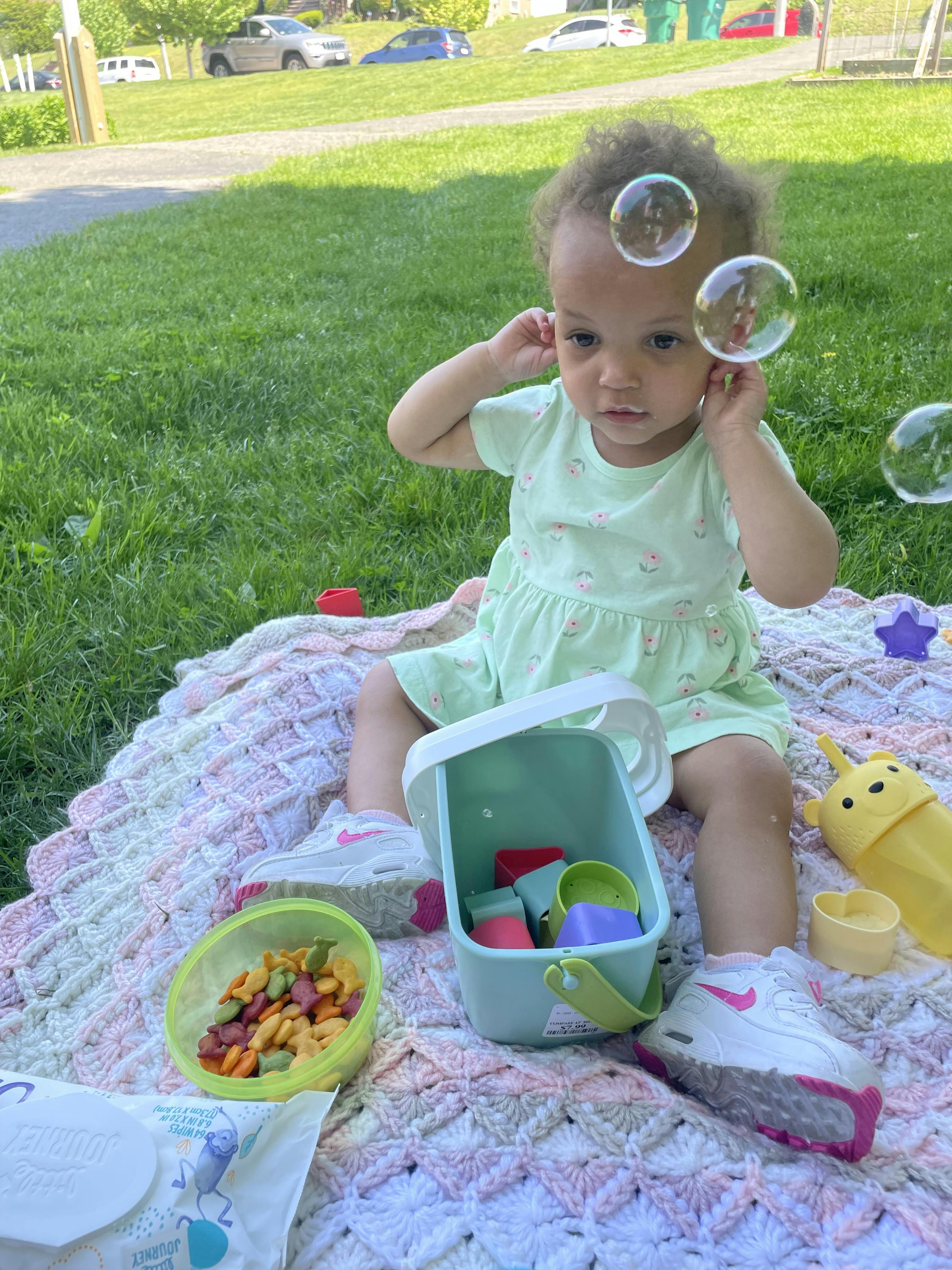 Child sitting on a blanket on grass with toys and bubbles