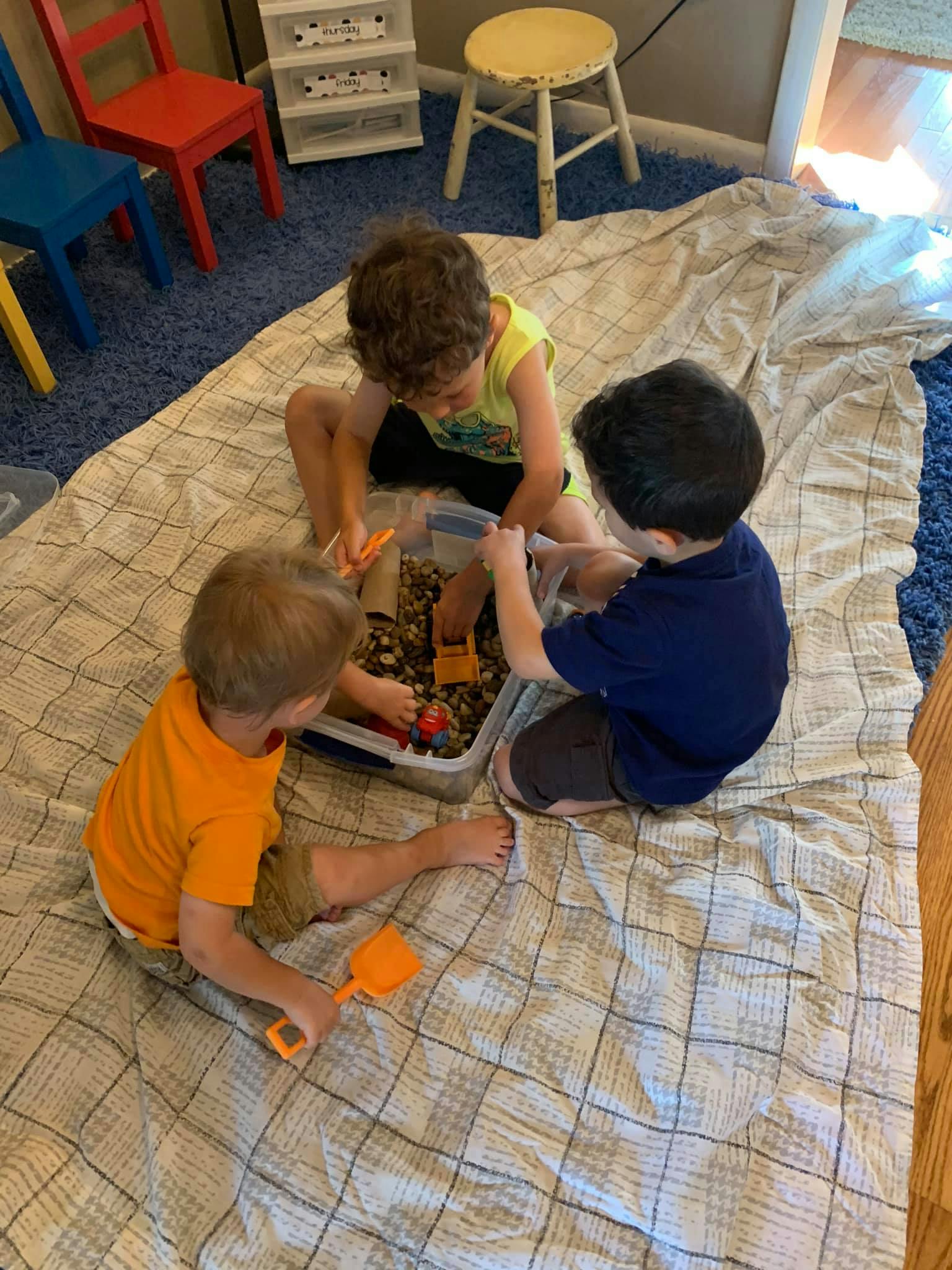 Three children playing with a sensory bin on a blanket