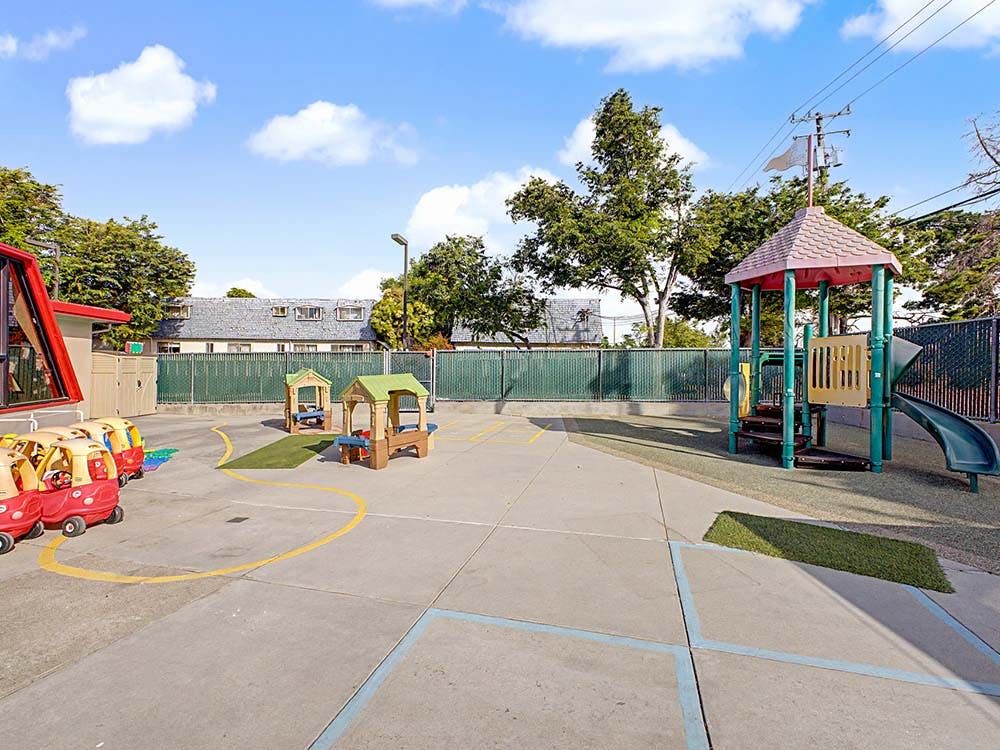Outdoor playground with ride-on cars, small picnic tables, and a slide structure