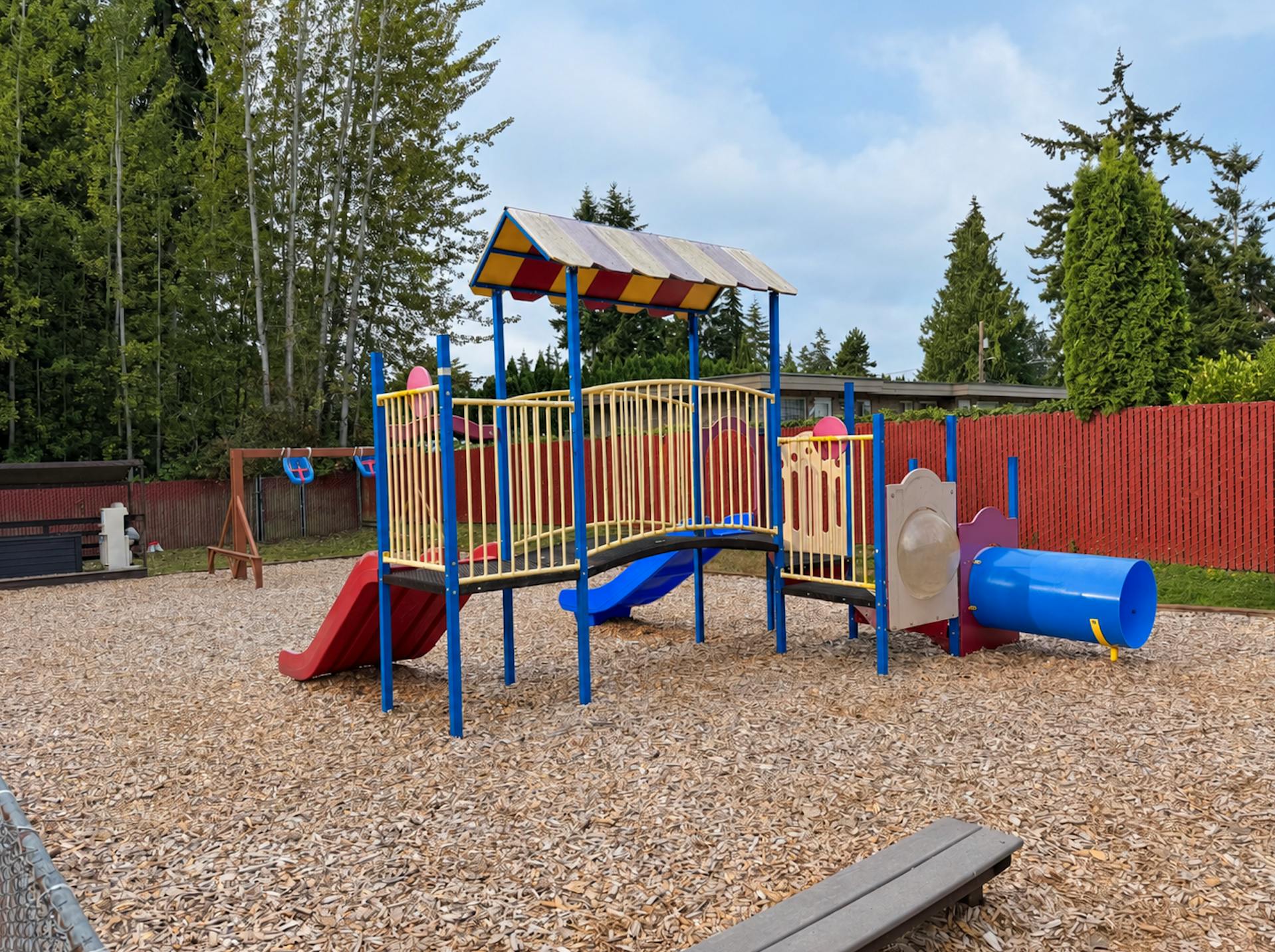 Playground structure with slides and a tunnel on a wood chip surface