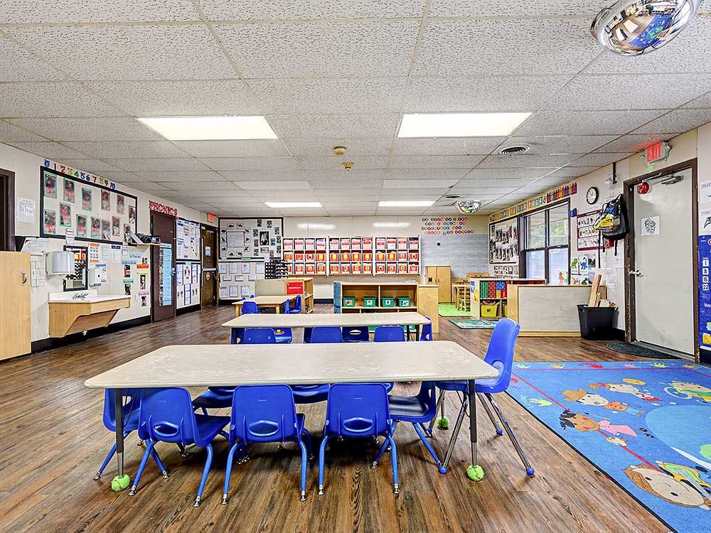 Classroom with small tables and chairs, colorful rugs, and learning materials