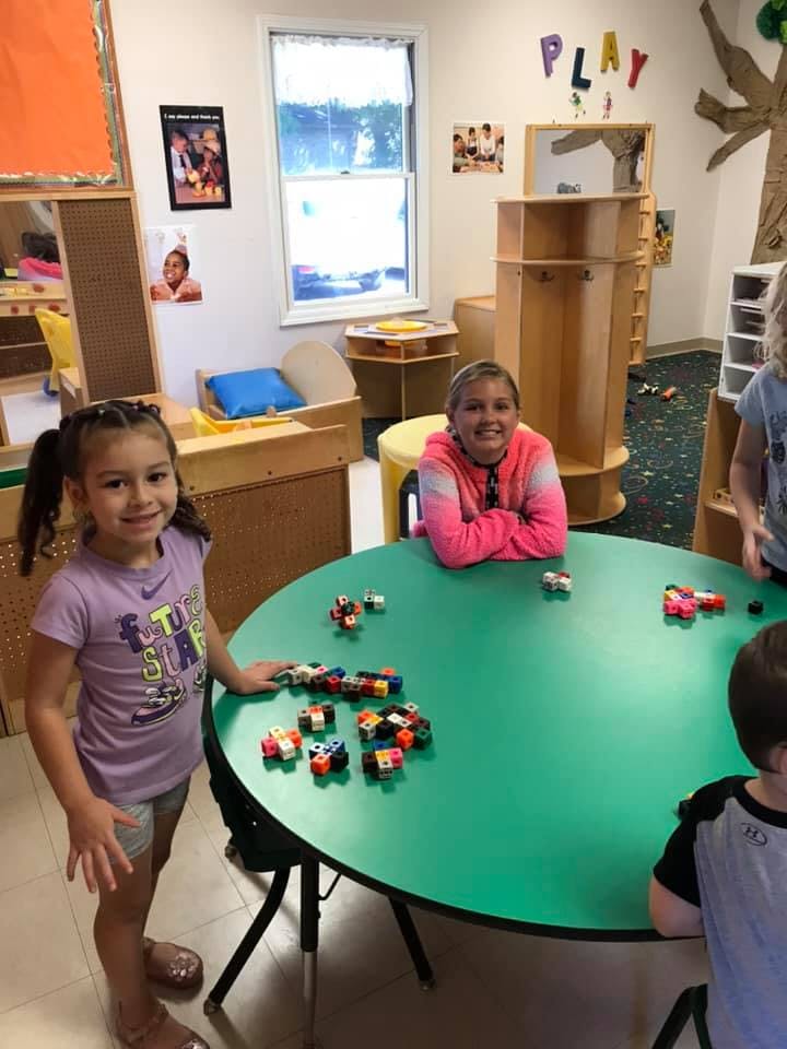 Two children playing with building blocks at a green table in a classroom