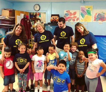 Four adults and multiple children posing in a classroom