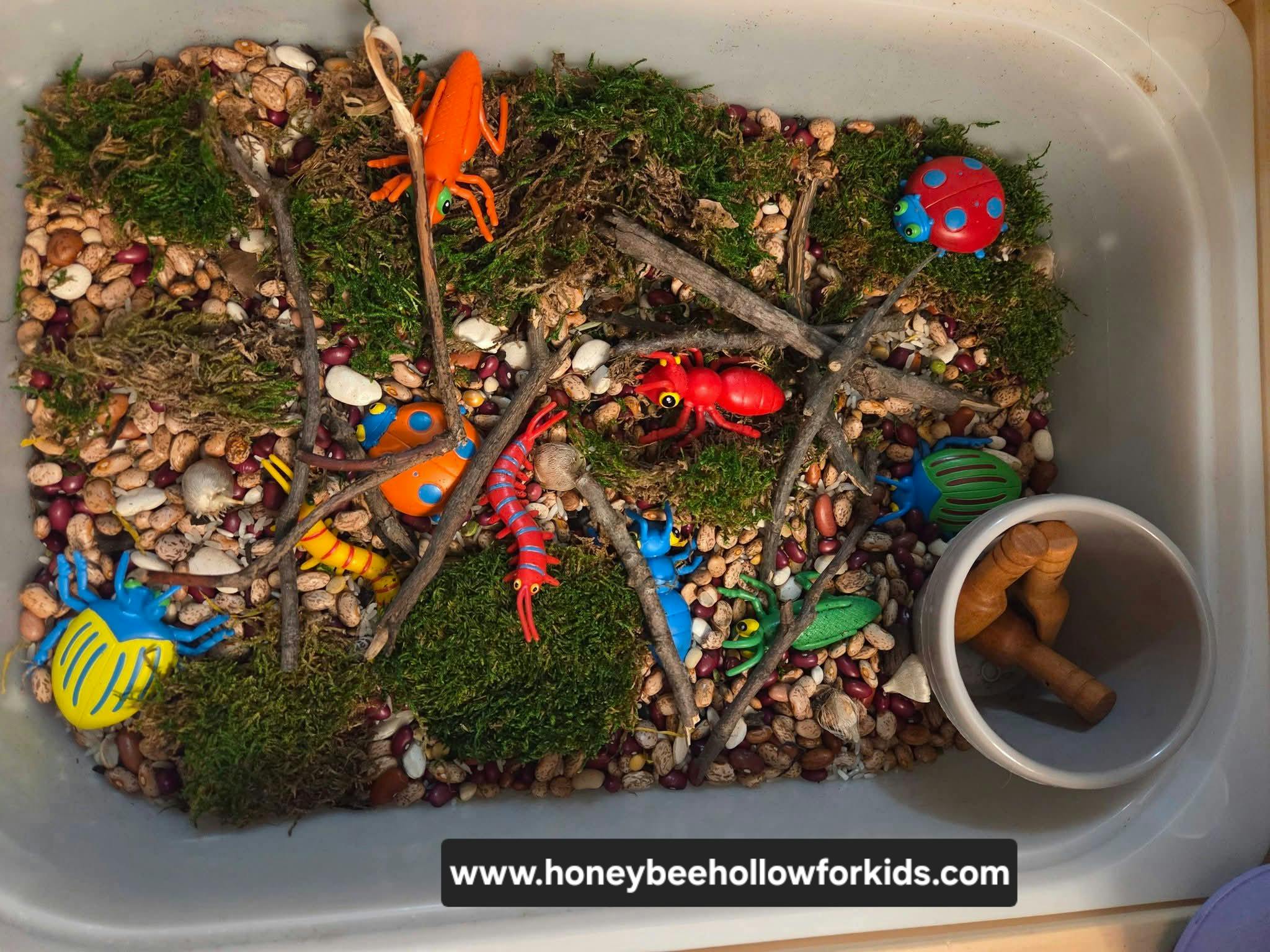 Plastic insect toys in a sensory bin filled with beans and moss