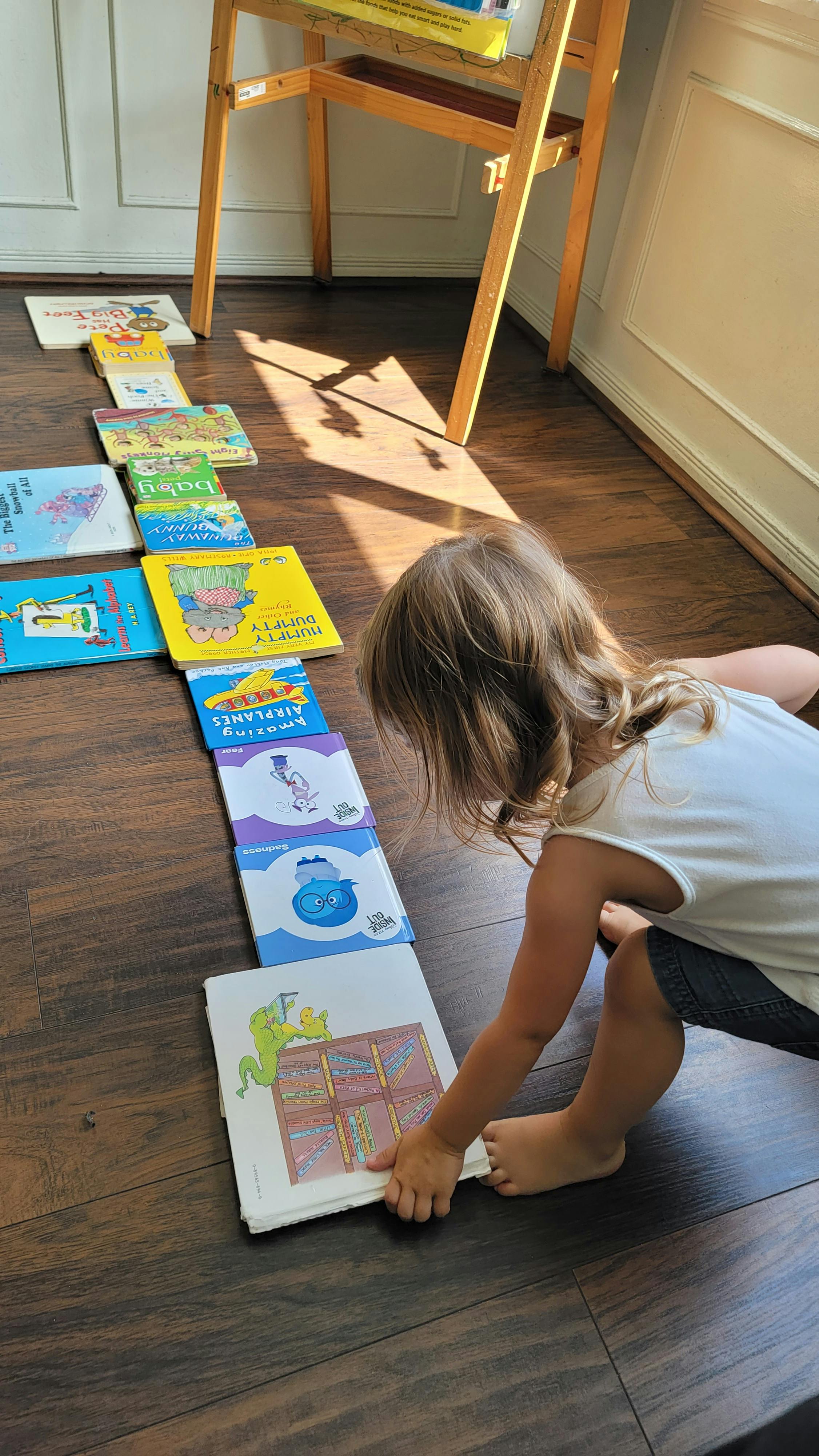 Child playing with a line of books on a wooden floor