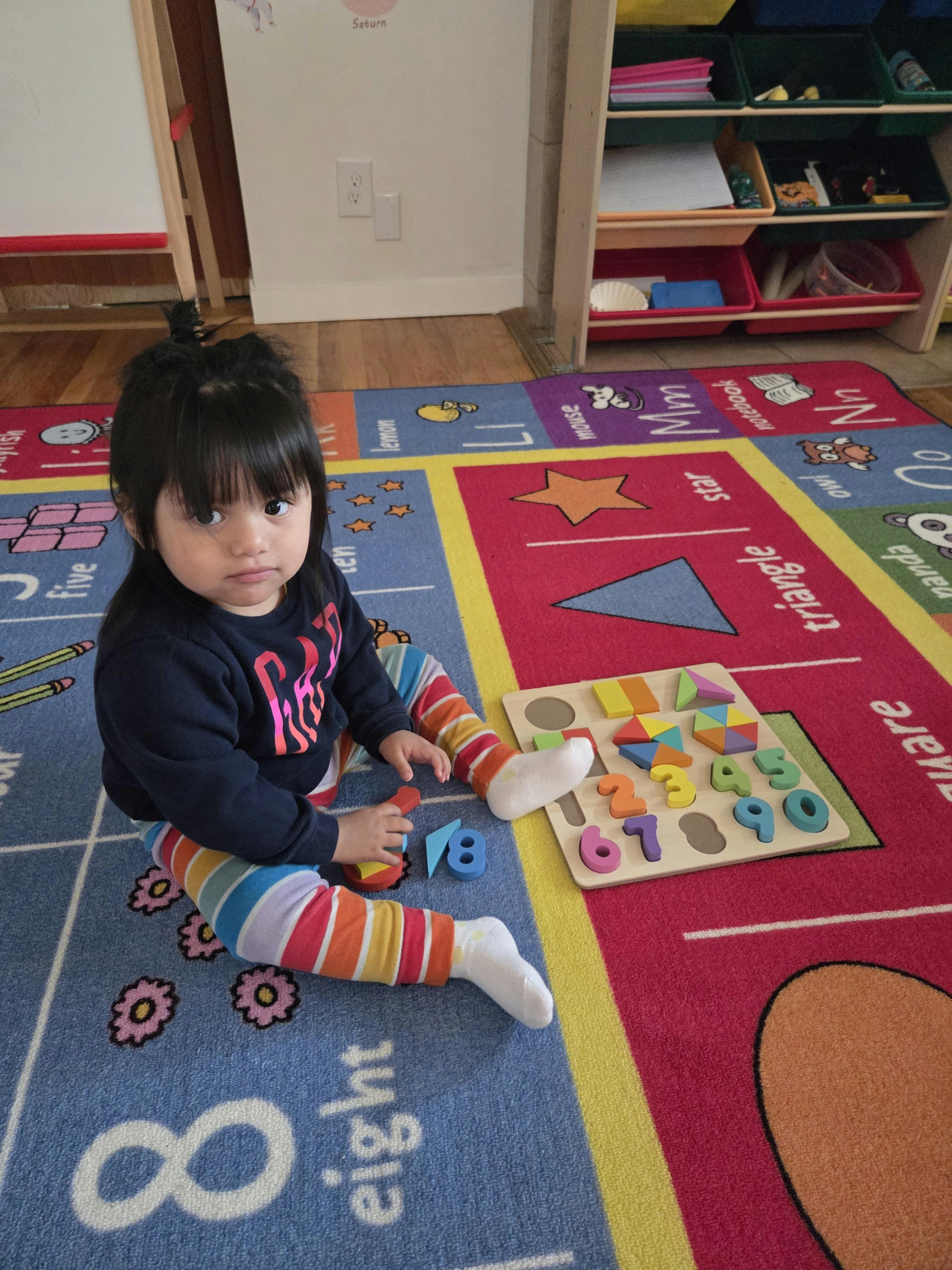 Child sitting on a colorful rug playing with a wooden number and shape puzzle