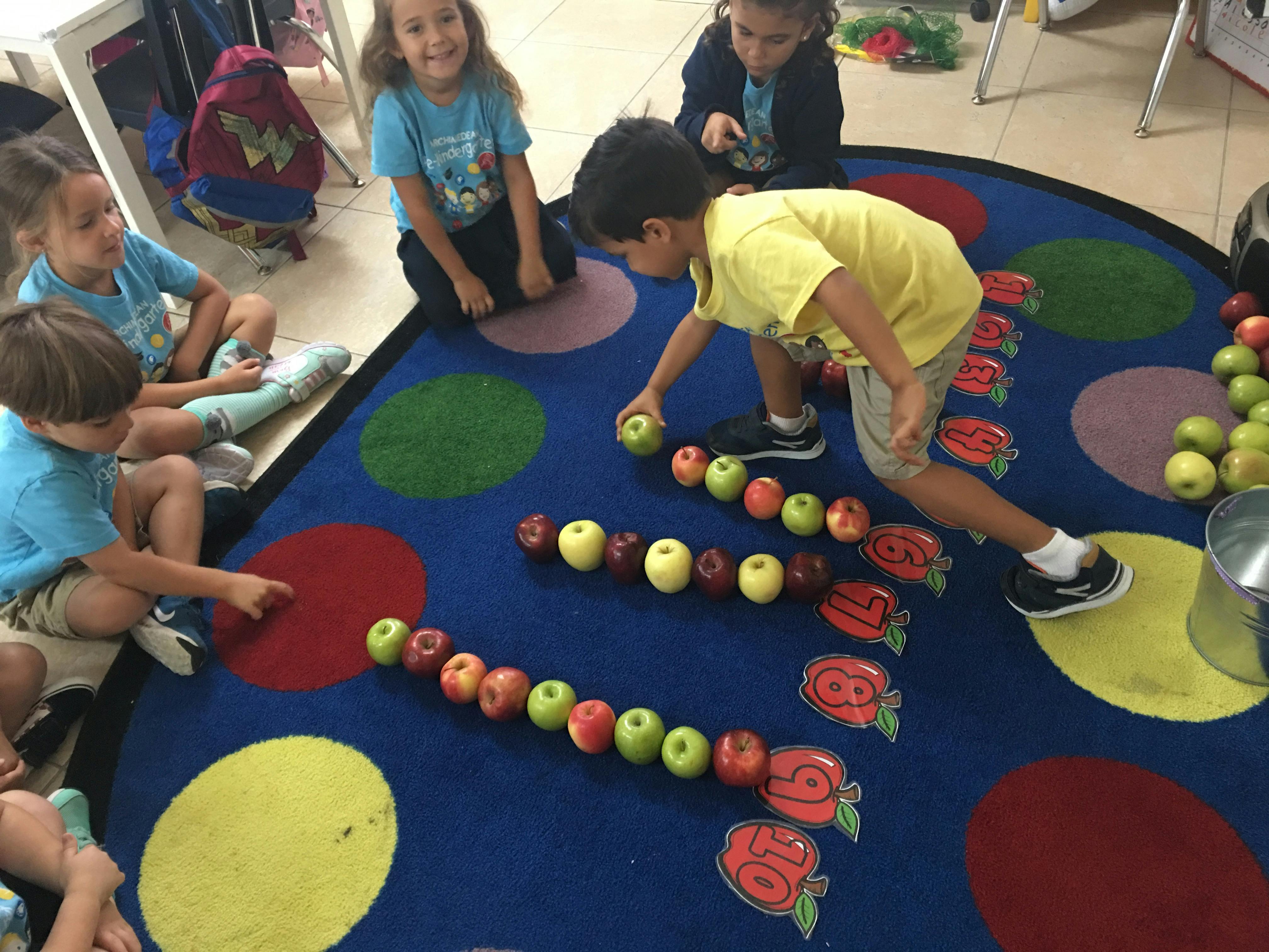 Children arranging apples in rows on a colorful rug