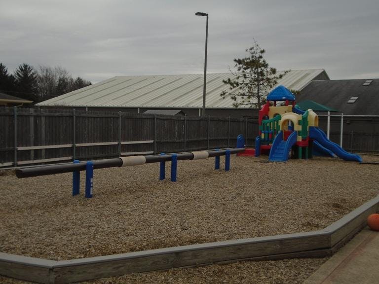 A wooden fence behind a colorful playground with slides and a balance beam
