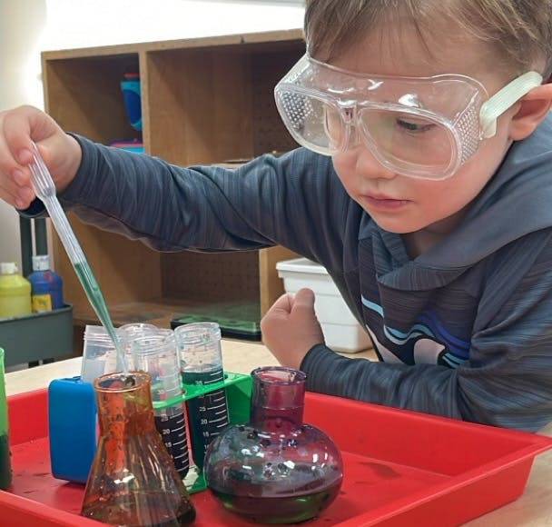 Child in safety goggles using a dropper with beakers