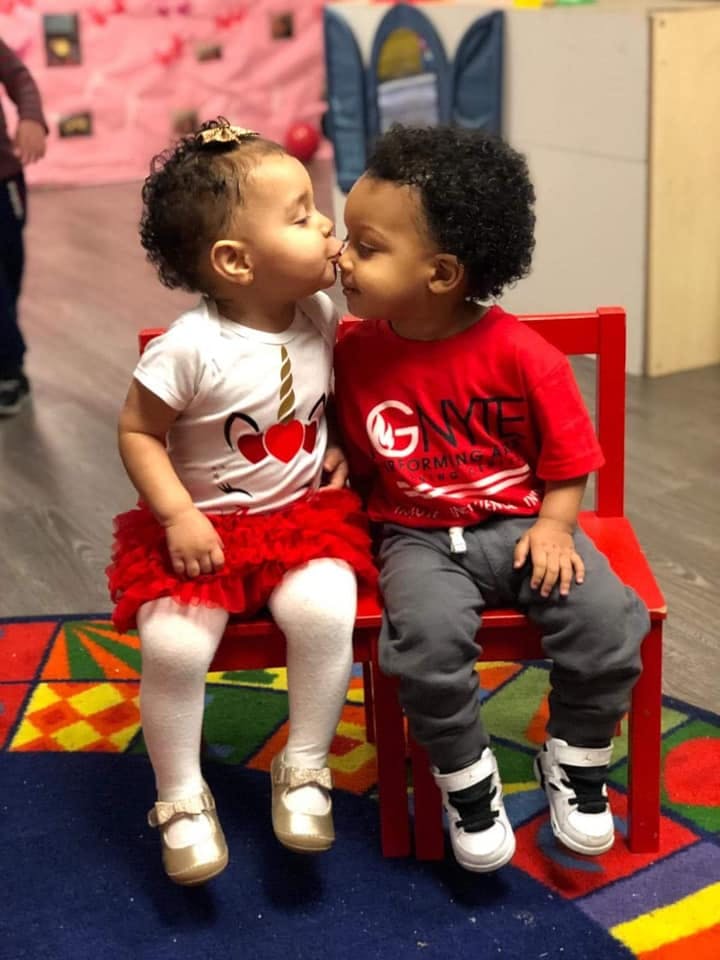 Two children sitting on a red chair, touching noses