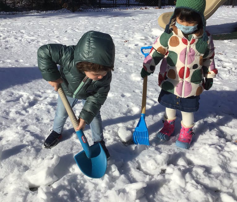 Two children playing in snow with a shovel and a rake