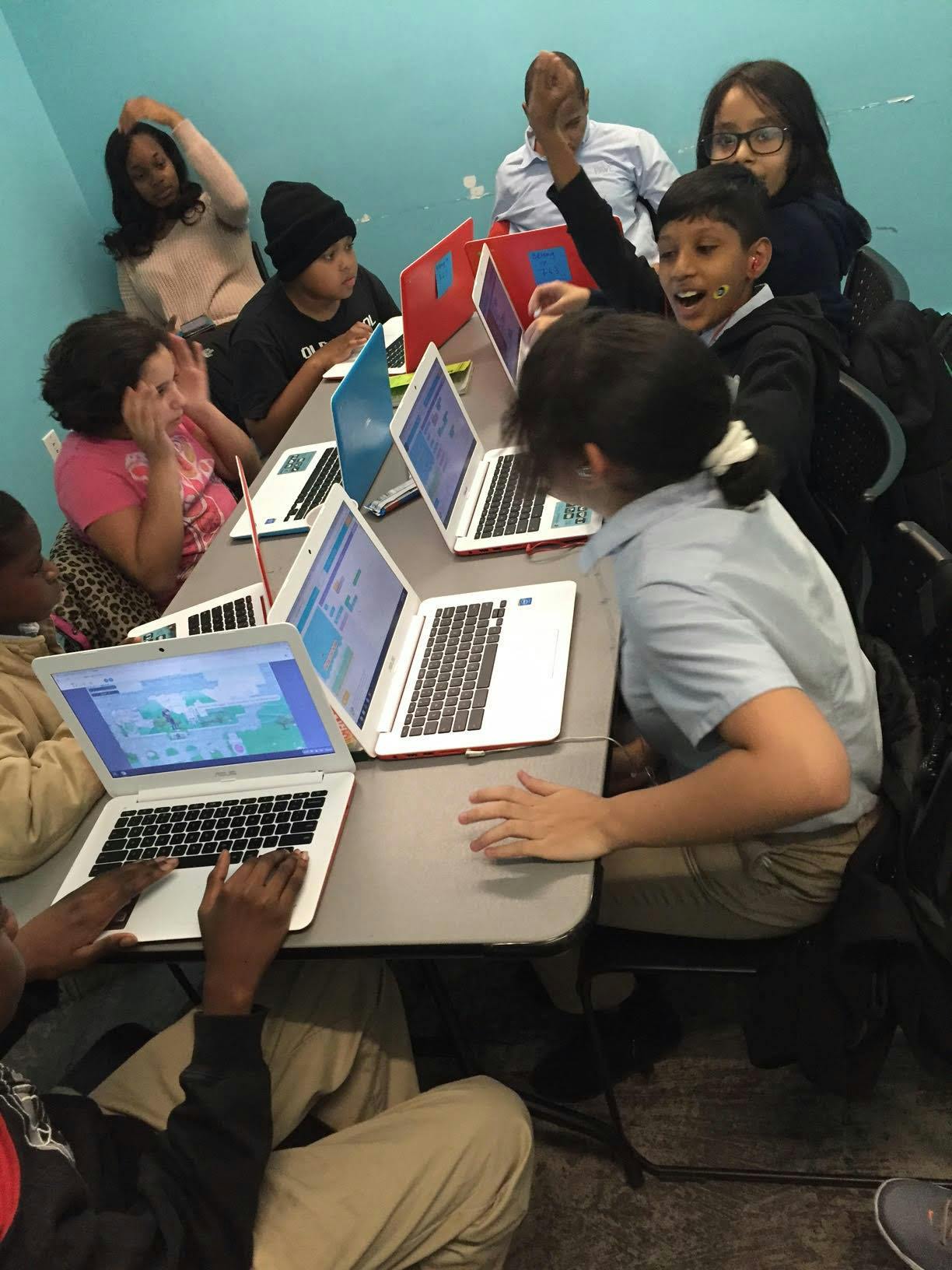 Group of people and children working on laptops at a table