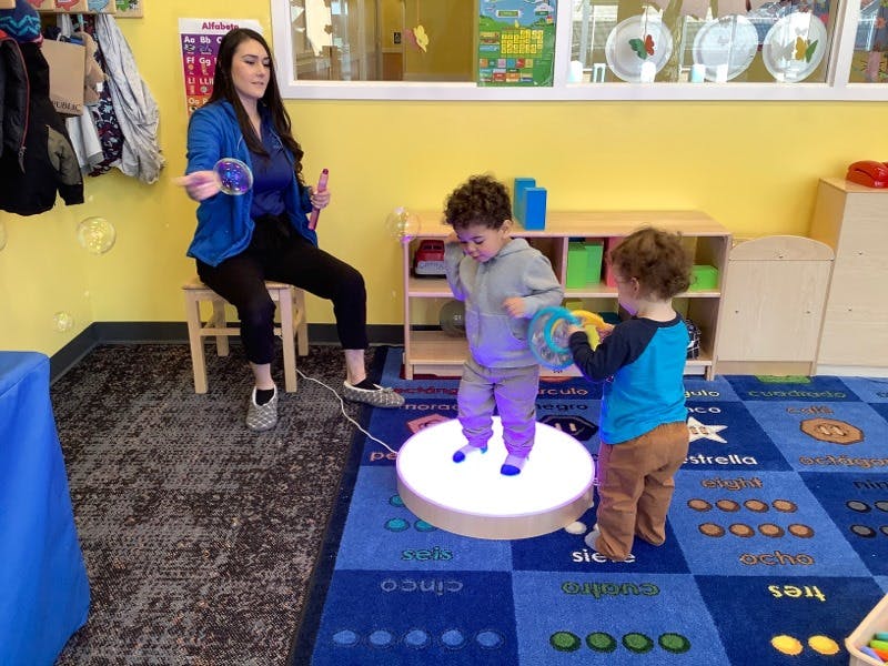 Person making bubbles while two children play on a light-up platform