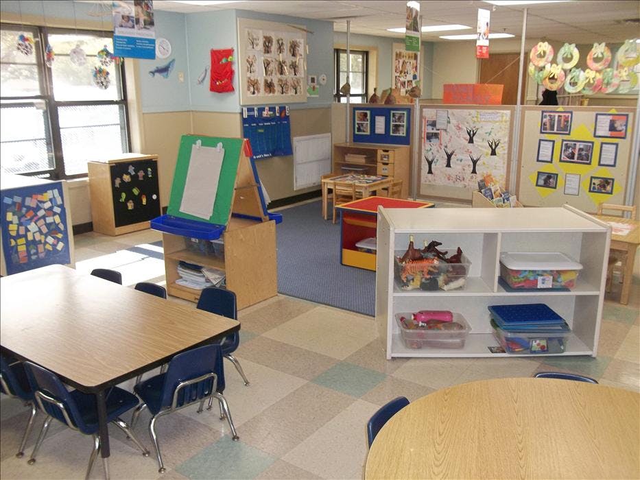 An empty early childhood classroom with small tables and chairs