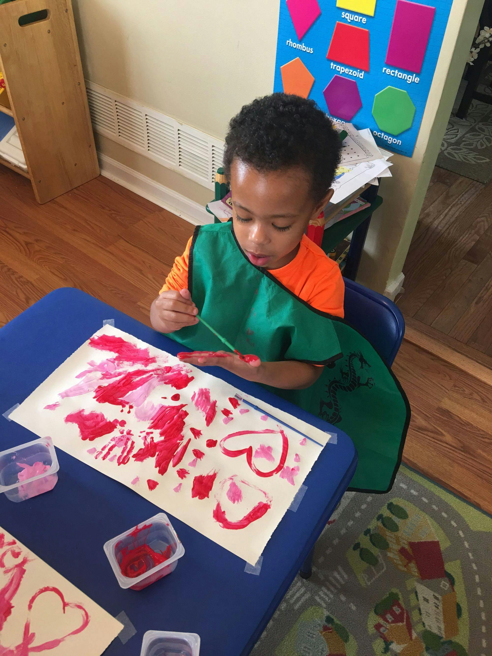 Child in a green smock painting with red paint at a table