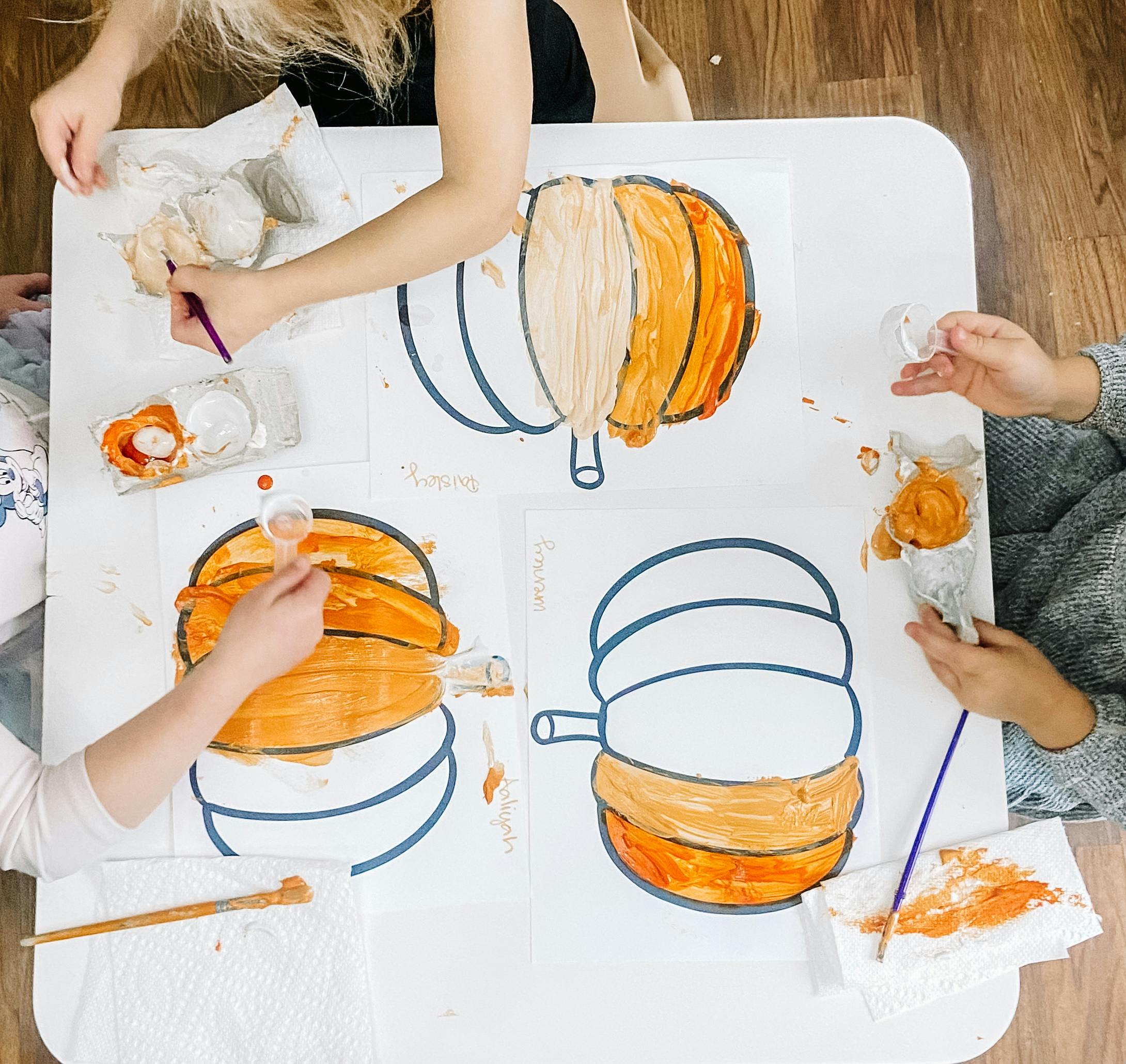 Multiple people painting pumpkin outlines with orange and white paint