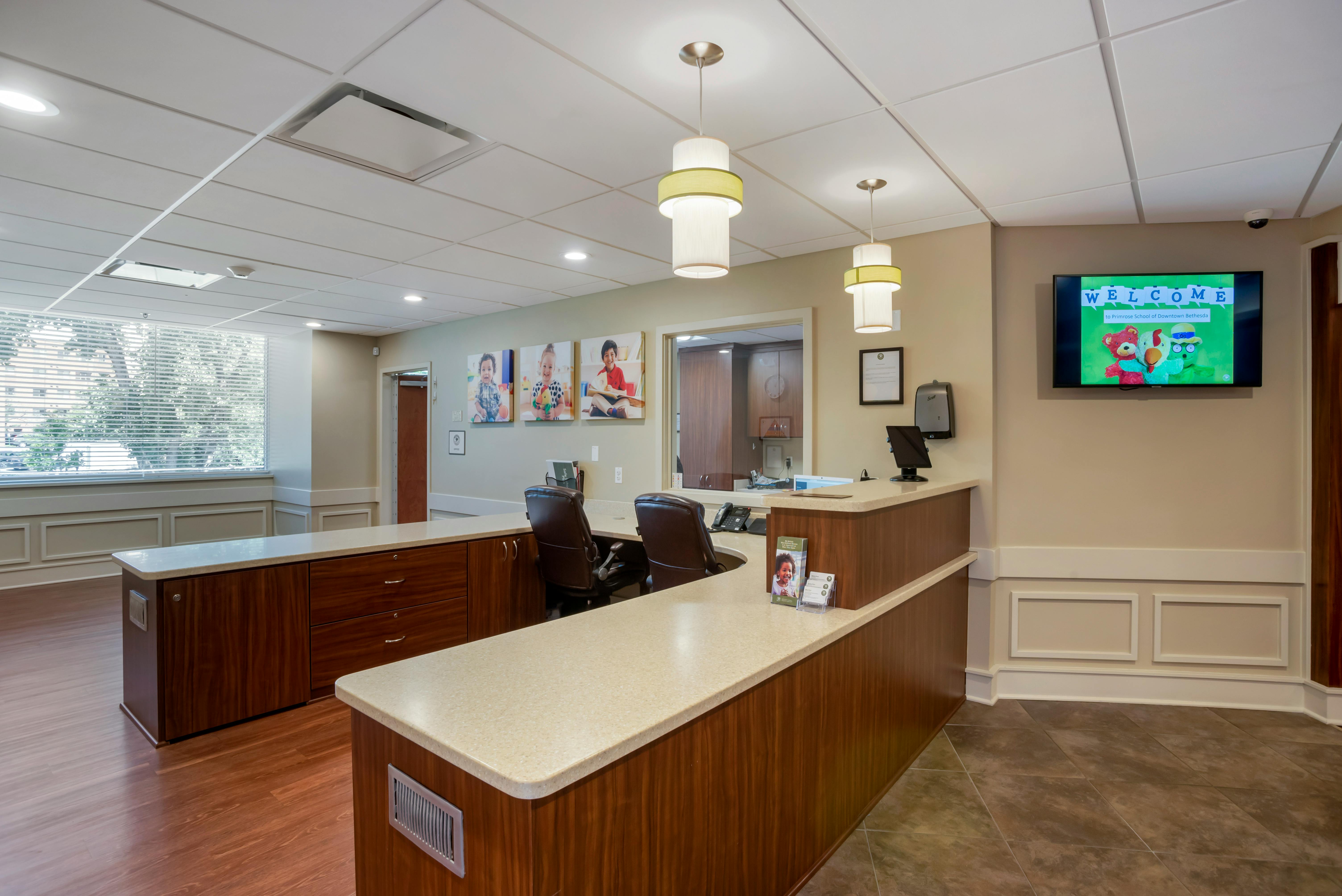Reception area with a light-colored counter, two chairs, and a monitor displaying "Welcome"